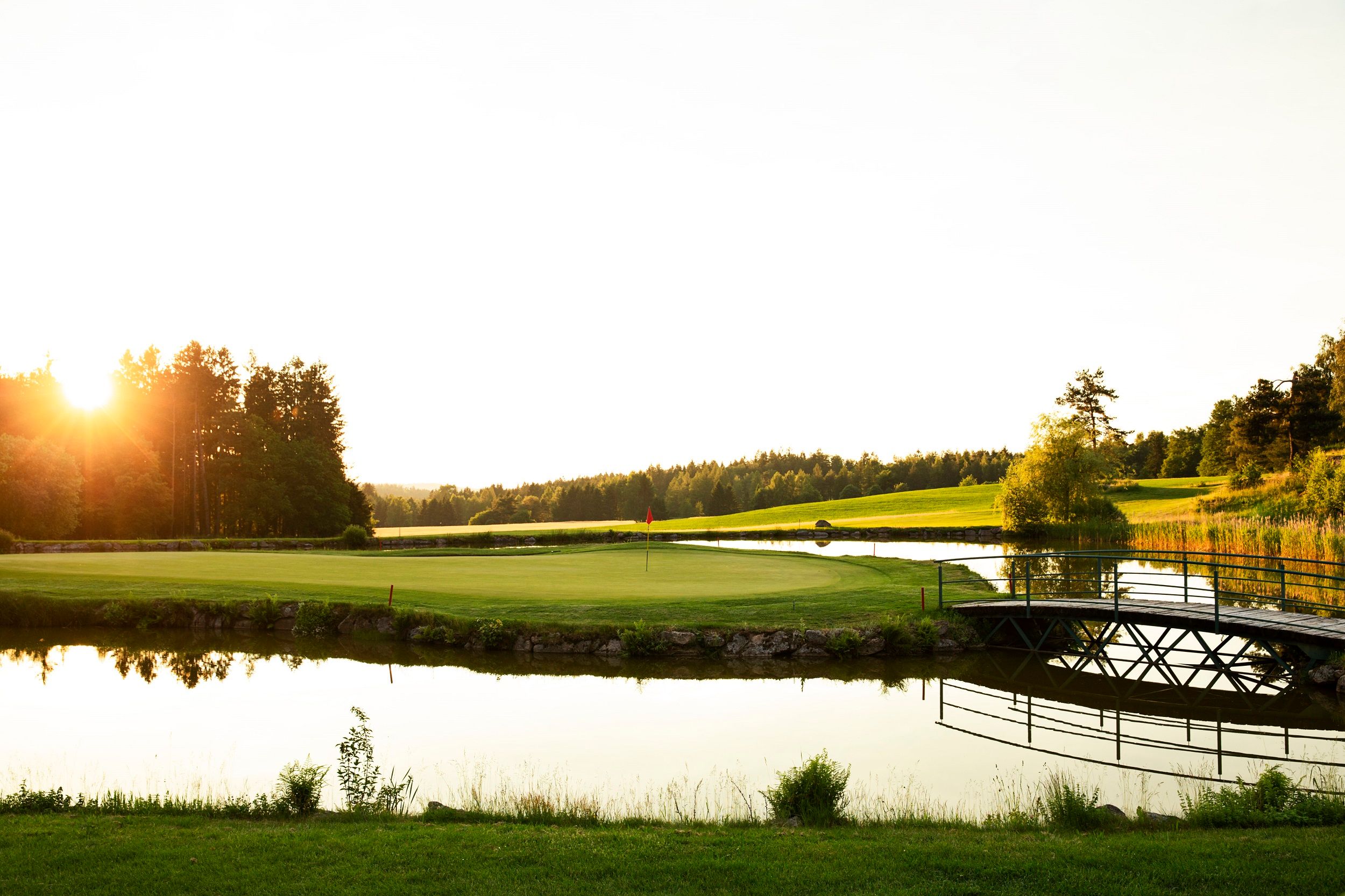 Golfplatz mit Teich und Brücke bei Sonnenuntergang im Golfresort Haugschlag.
