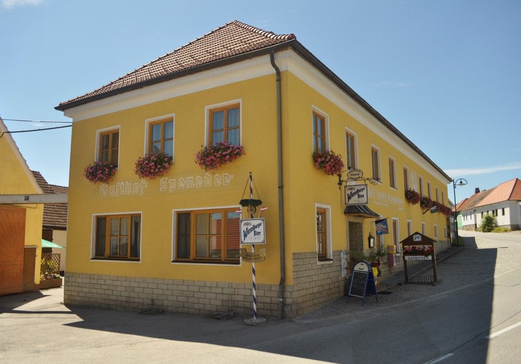 Gelbes Gebäude mit der Aufschrift 'Gasthof Speneder', dekoriert mit Blumen.