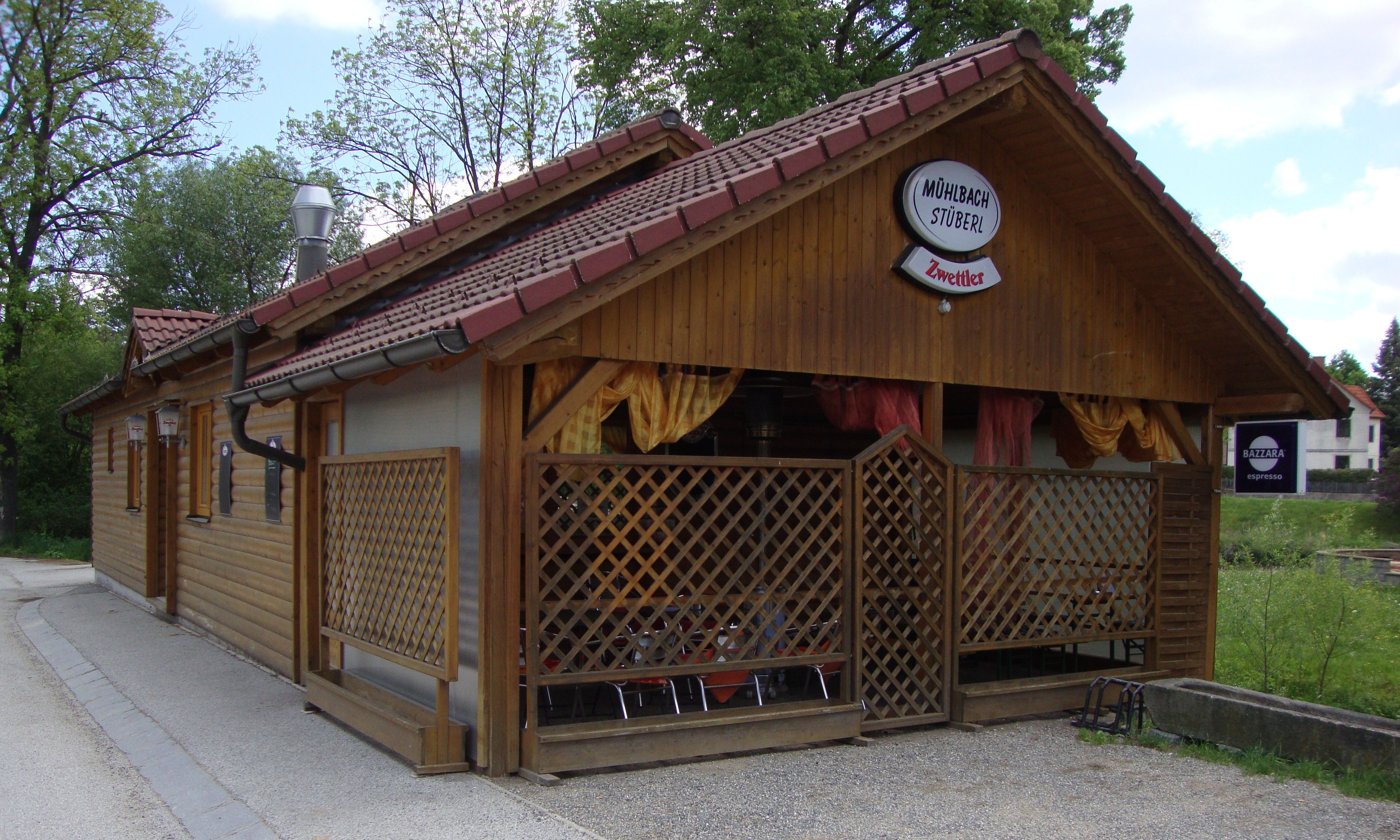 Holzgebäude mit Schild 'Mühlbachstüberl' und 'Zwettler' Logo, umgeben von Bäumen.