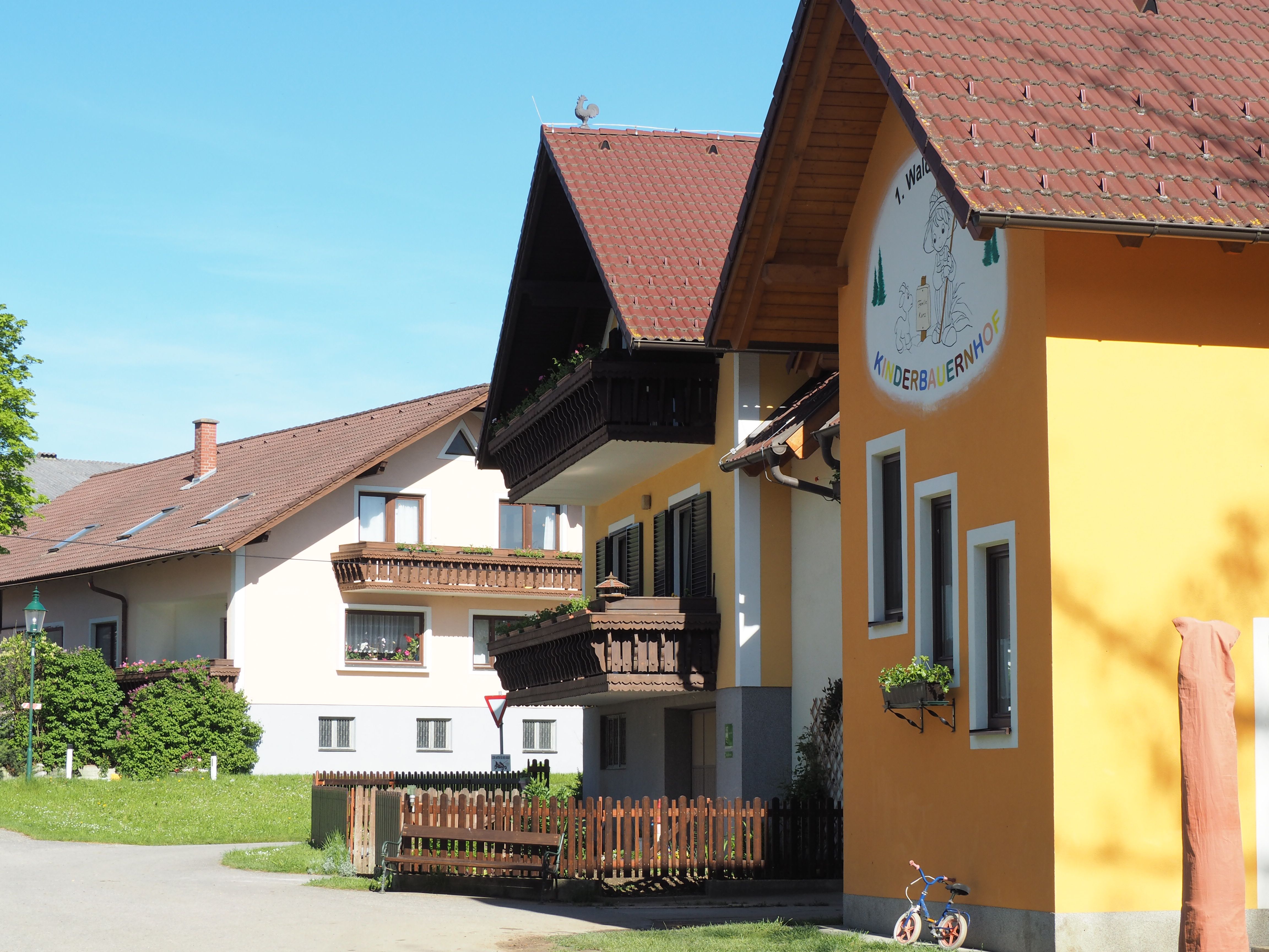 Gebäude des Waldvierteler Kinderbauernhofs mit gelber Fassade und Holzbalkonen, umgeben von grüner Landschaft.