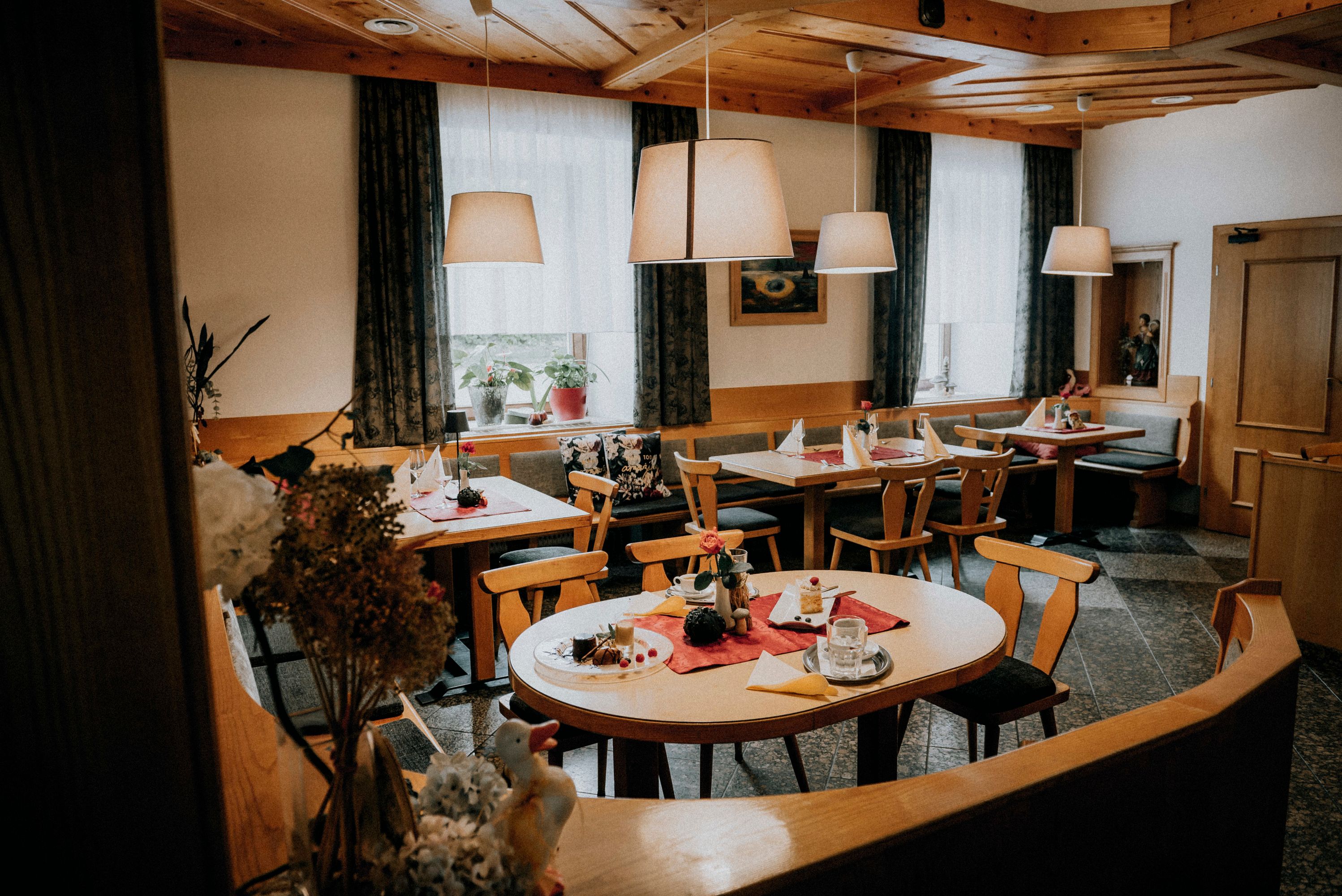Gemütlicher Gastraum mit Holzmöbeln, gedeckten Tischen und Hängelampen.
