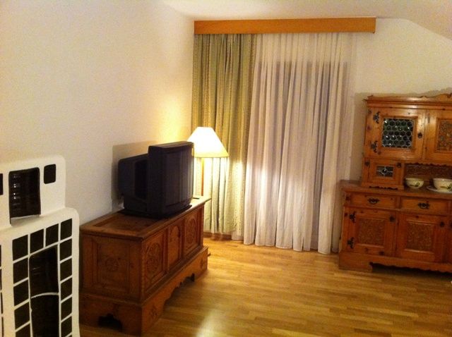 Ein Wohnzimmer mit Holzmöbeln, einem alten Fernseher, einer Stehlampe und Vorhängen.