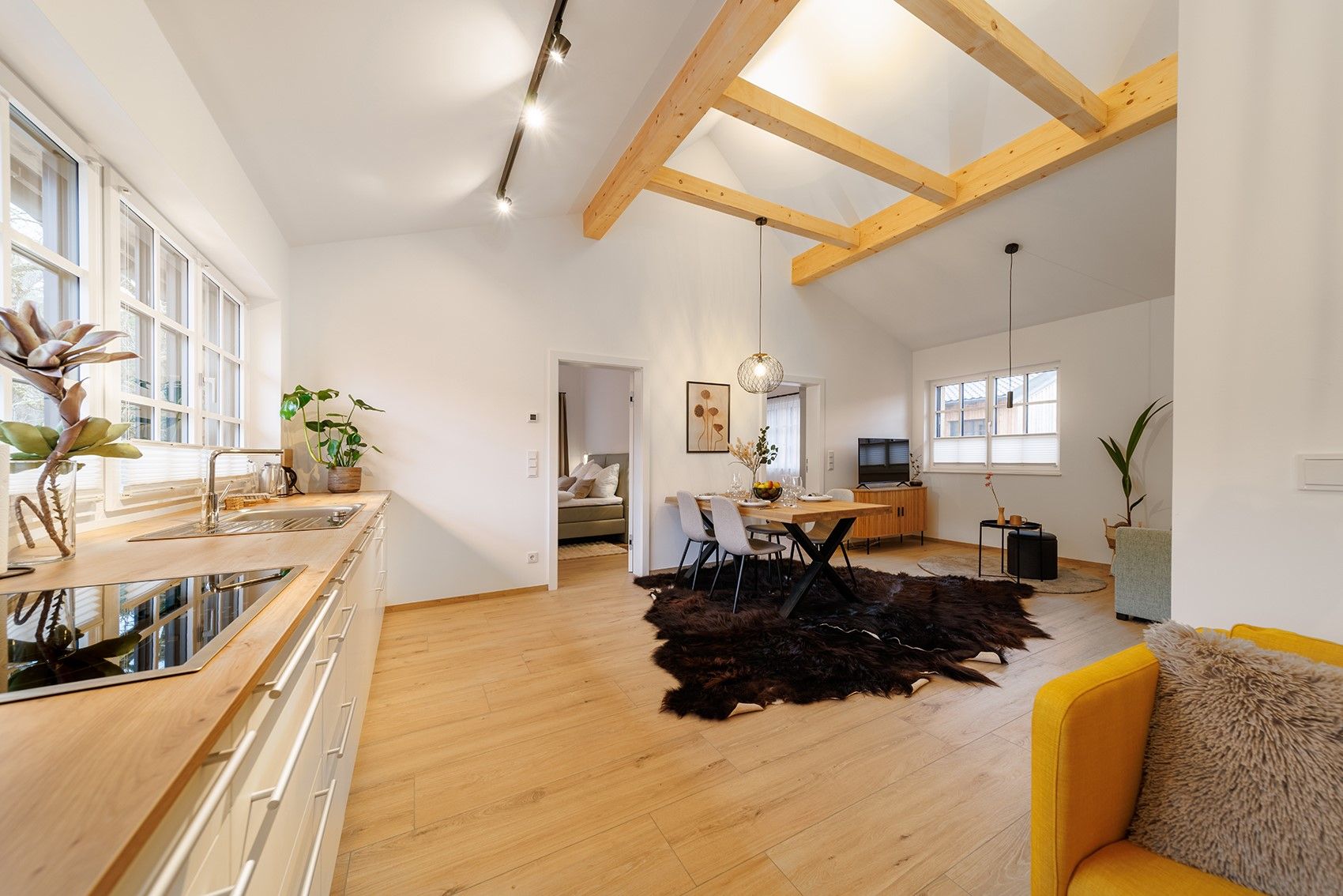Modernes Wohnzimmer mit Holzbalken, Esstisch, gelbem Sessel und offener Küche.