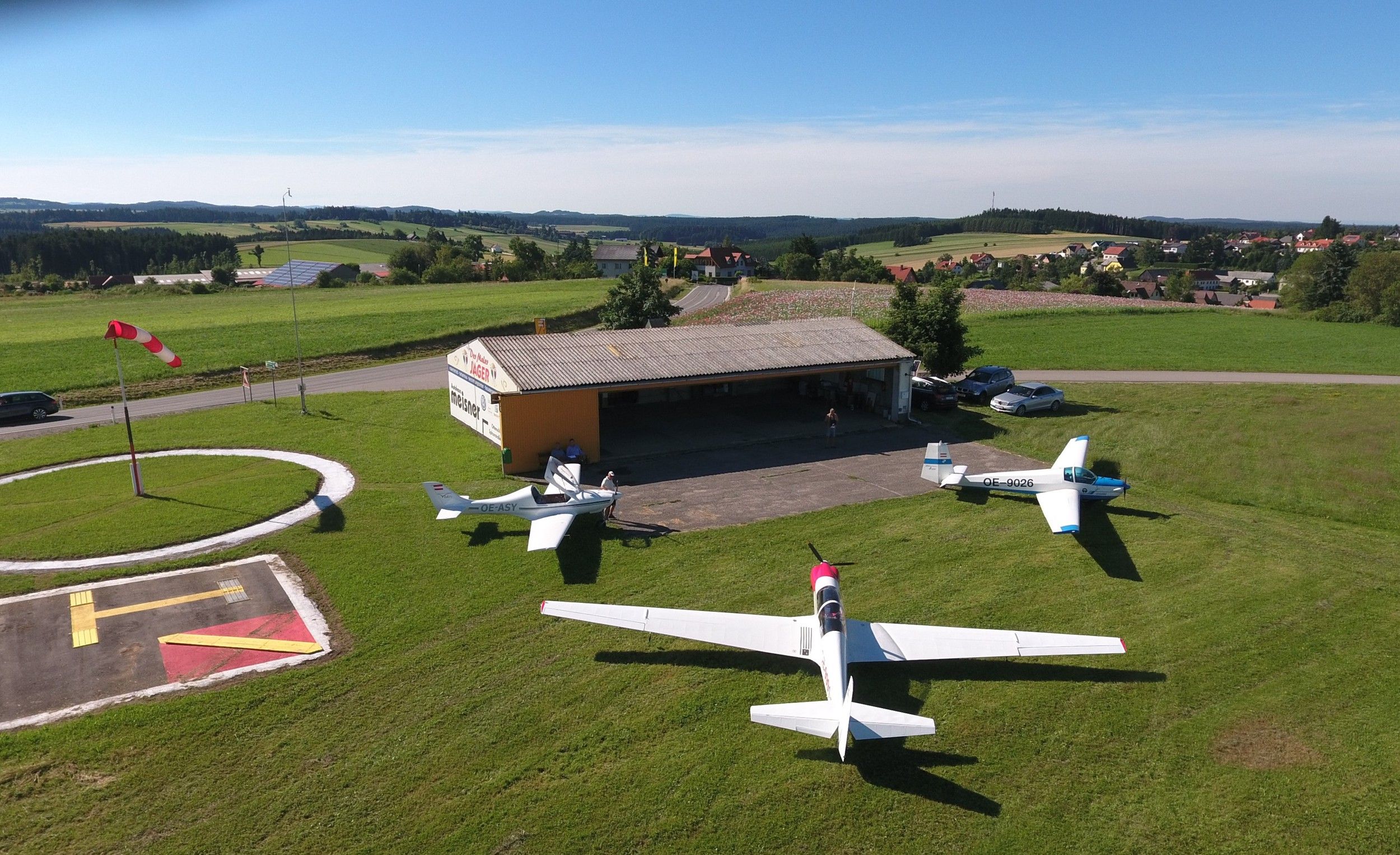 Landschaft mit Flugplatz, Segelflugzeugen und Windsack.