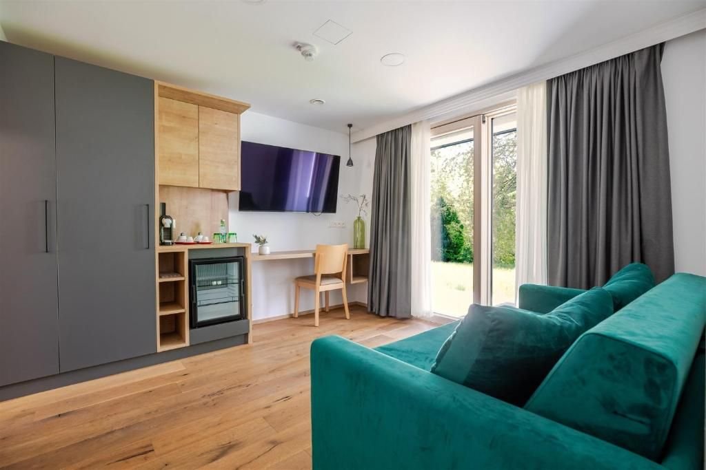 Hotelzimmer im Hotel Ottenstein – Das Wohlfühlhotel mit grünem Sofa, Schreibtisch, TV, Schrank und Blick ins Grüne.
