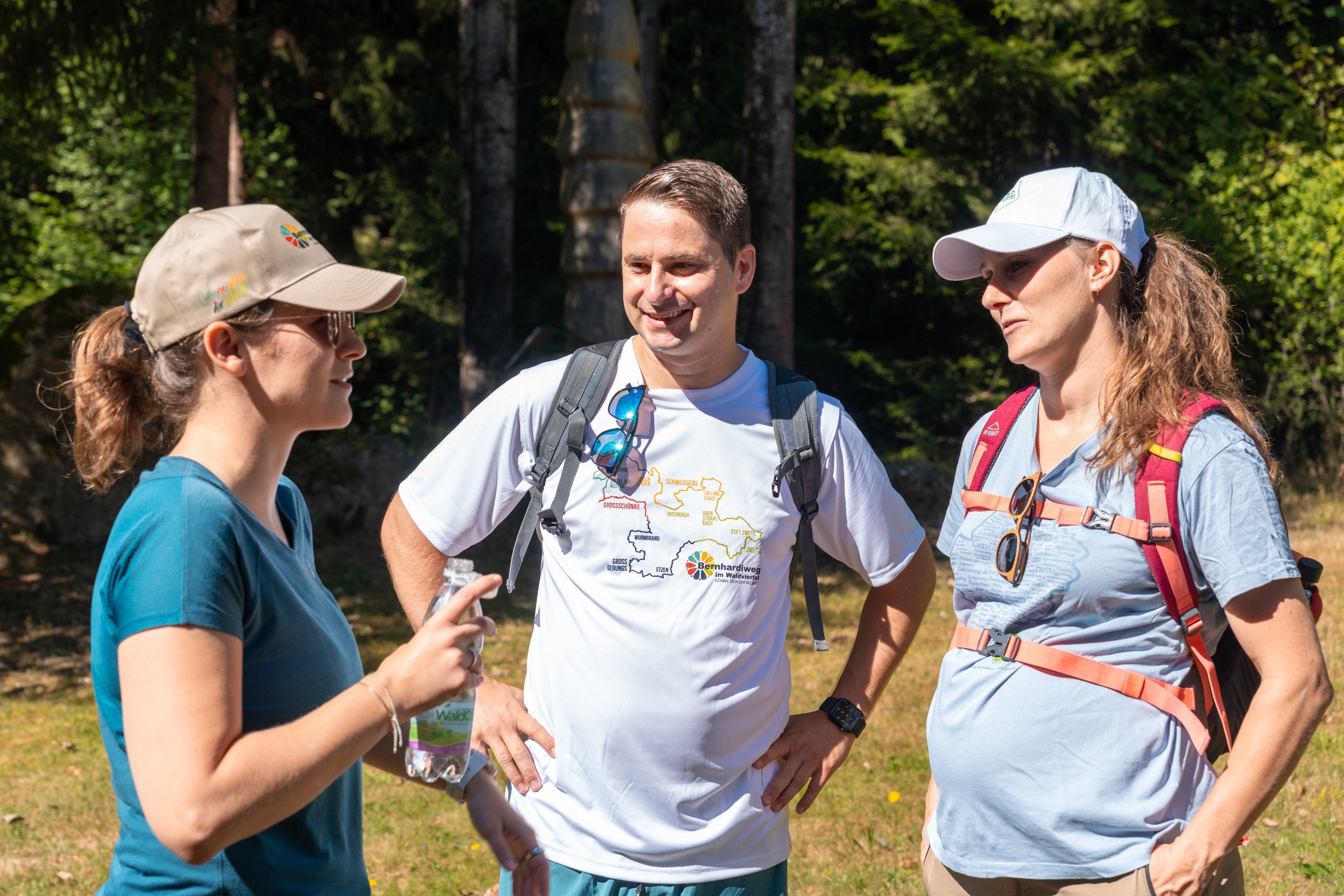 Ein Mann und 2 Frauen auf einer Wiese. Im Hintergrund Wald.