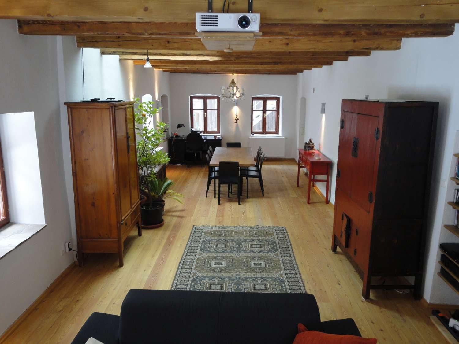 Ein stilvoll eingerichteter Raum mit Holzboden, Holzbalkendecke, antiken Möbeln und einem Teppich.