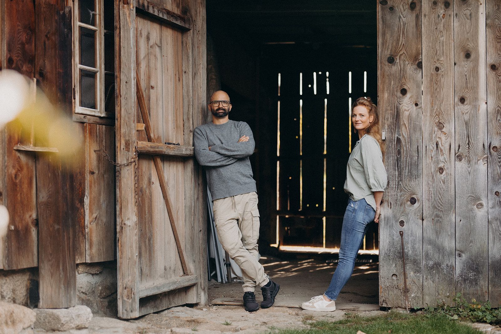Ein Mann und eine Frau lehnen lässig an den Holztüren einer Scheune.