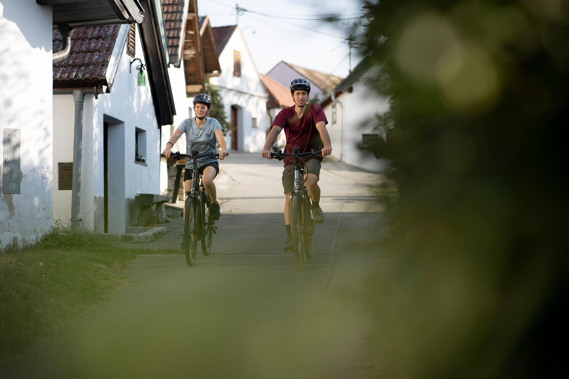Zwei Radfahrer genießen die sanfte Brise und die malerische Landschaft, während sie durch die charmanten Gassen radeln. Umgeben von idyllischen Weinbergen und historischen Kellergassen, spüren sie die entspannte Atmosphäre des Weinviertels.