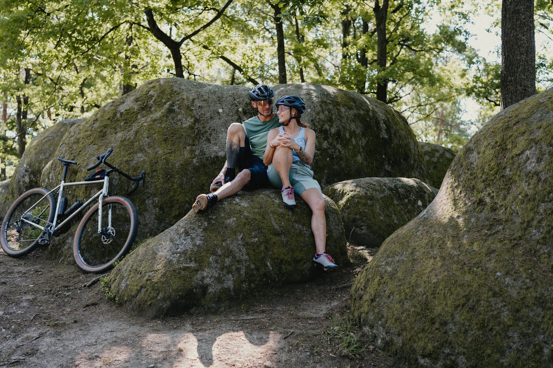 Ein Mann und eine Frau sitzen in Fahrradmontur auf einem Stein und unterhalten sich, neben ihnen auf einem weiteren Stein angelehnt ihre Räder