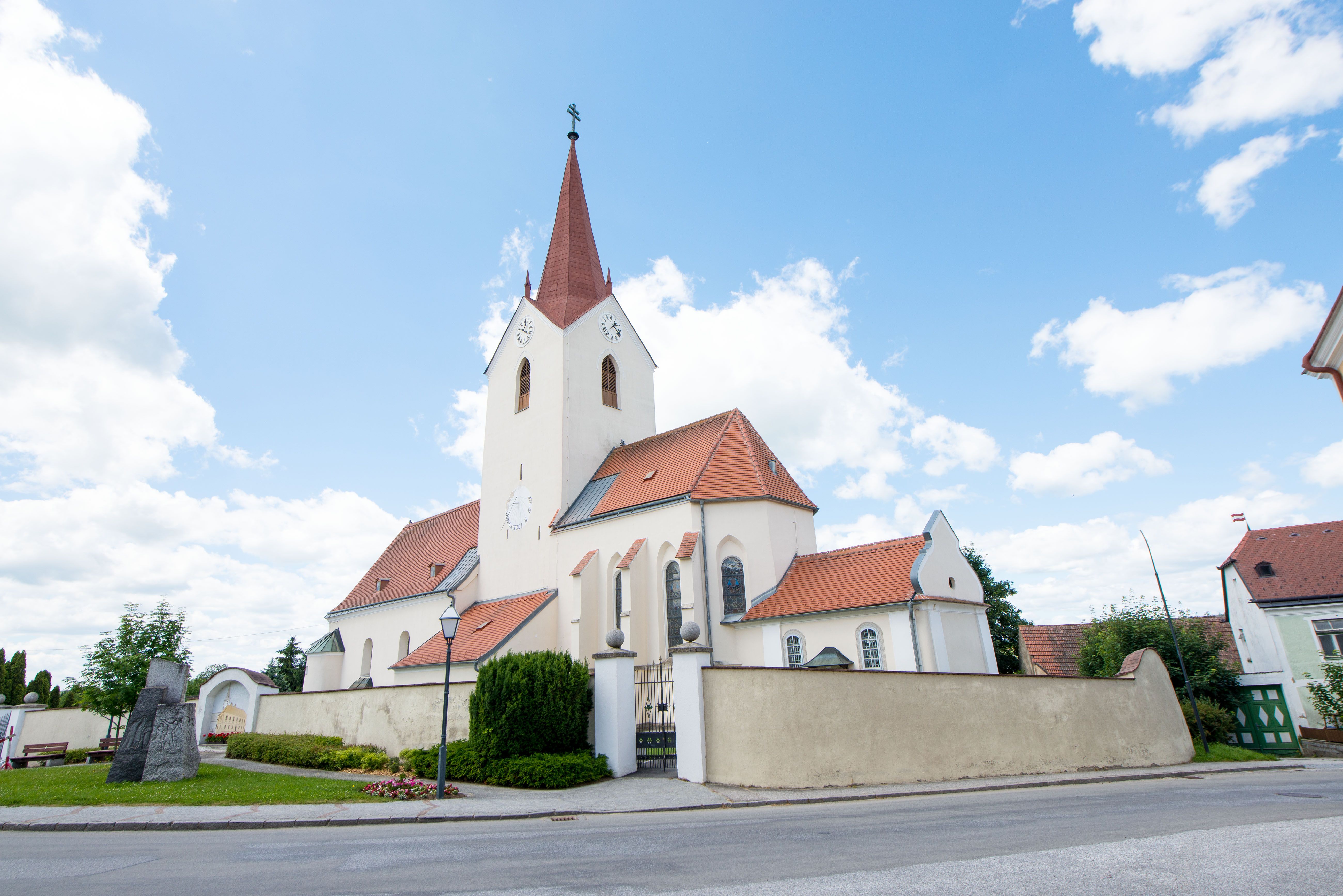 Eine Kirche in der Marktgemeinde Schweiggers. Davor eine Steinskulptur mit eingravierten Menschen.