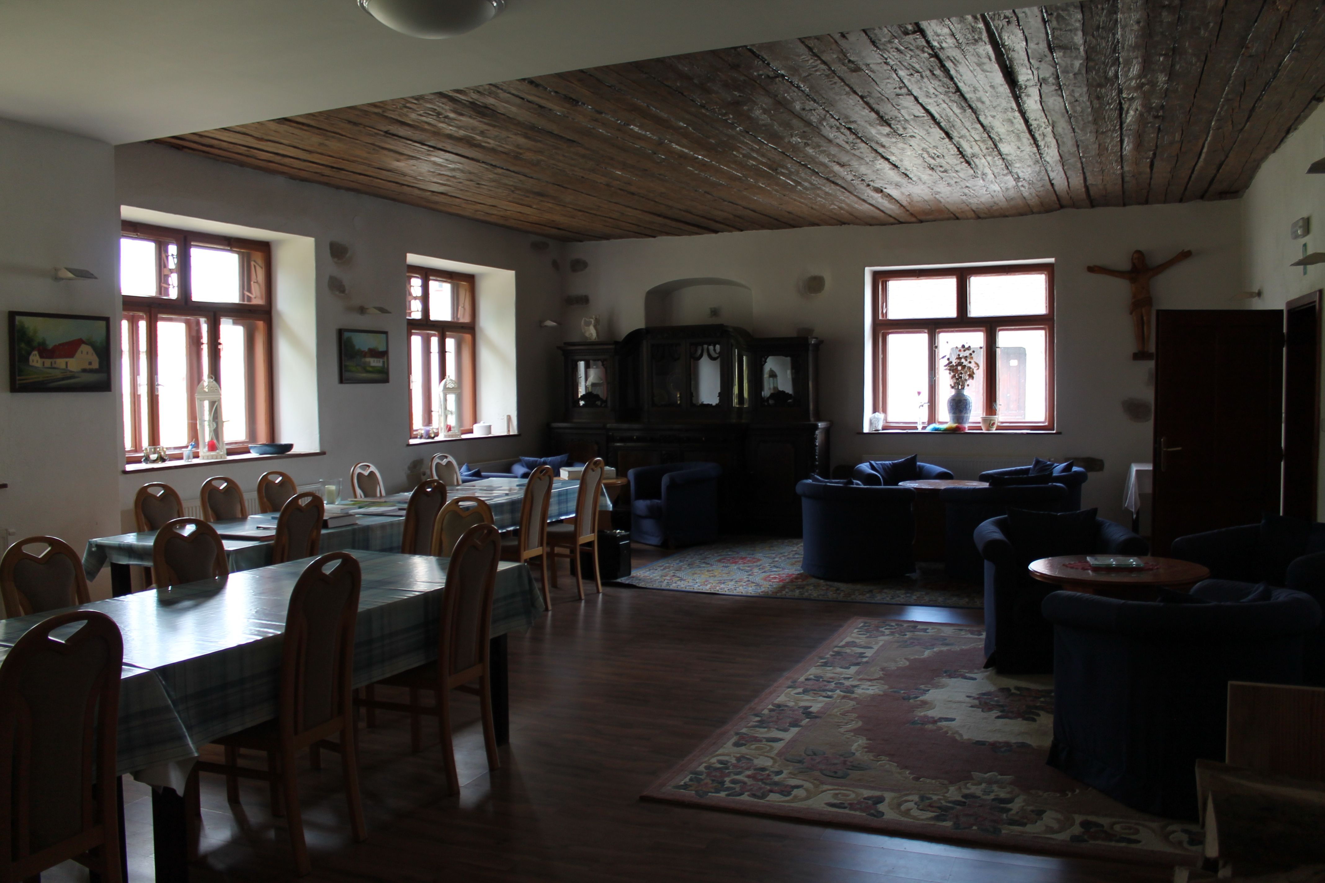 Ein gemütlicher Raum mit Holztischen, Stühlen und Sofas, dekoriert mit Teppichen und Bildern an den Wänden.