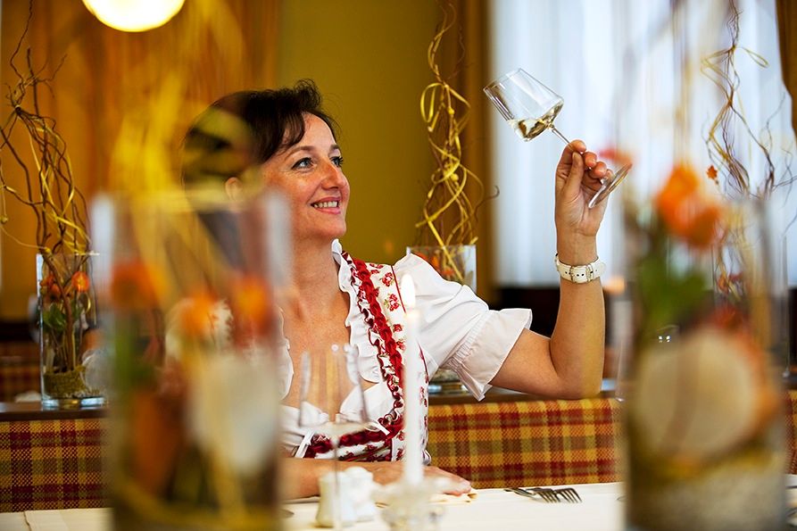 Frau in traditioneller Kleidung hält ein Weinglas in einem Restaurant.