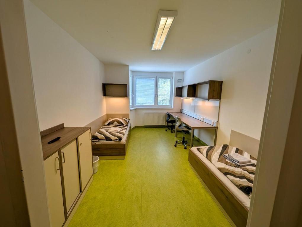 Ein einfach eingerichtetes Zimmer mit zwei Betten, Schreibtischen und einem Fenster.