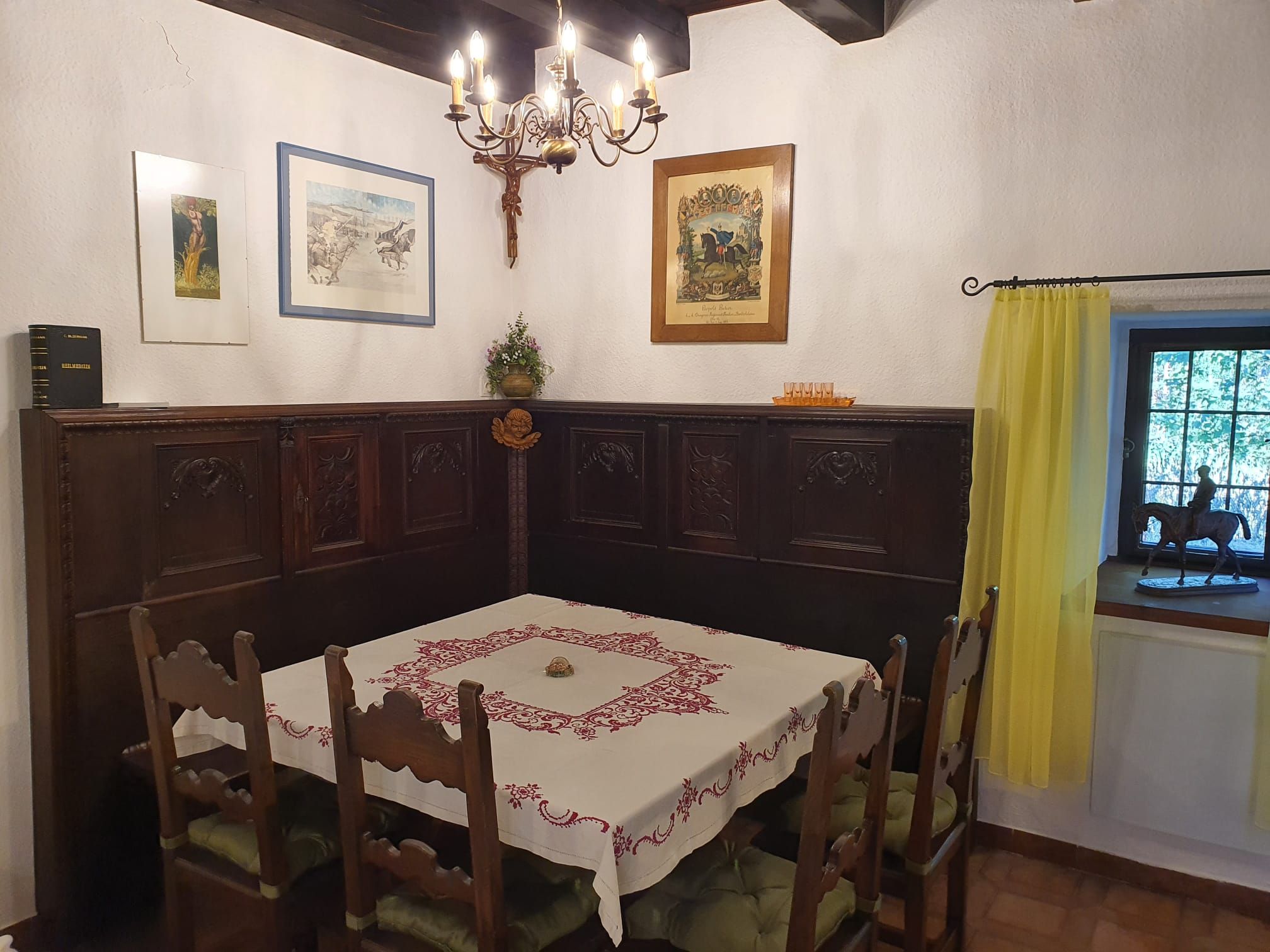 Gemütliche Essecke mit Holzmöbeln, Tischdecke und Wanddekorationen in einem rustikalen Raum.