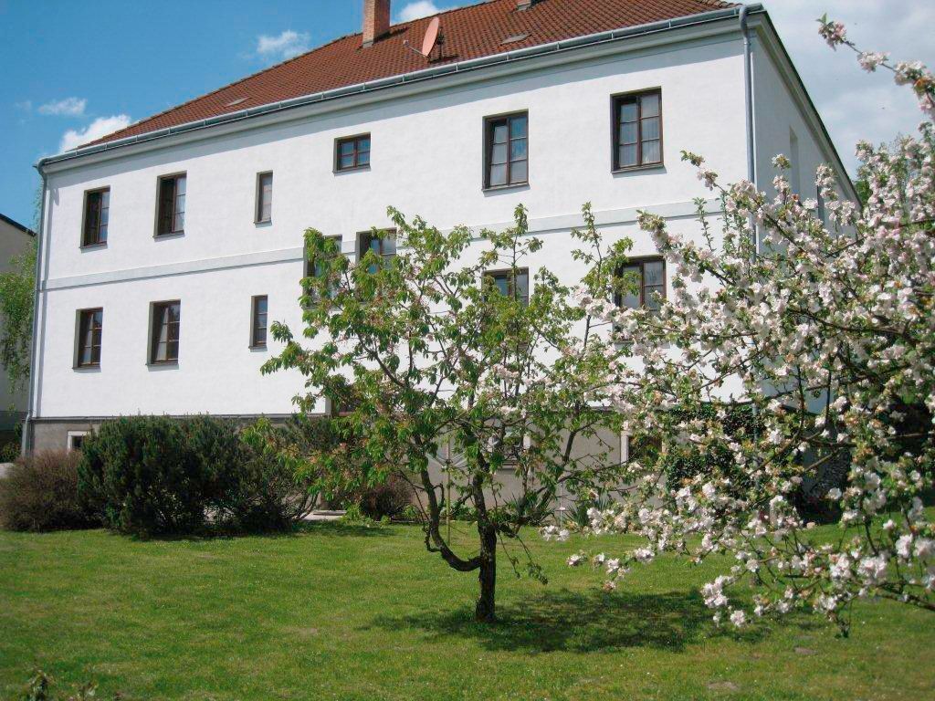 Ein weißes Gebäude mit braunem Dach und blühenden Bäumen im Vordergrund.
