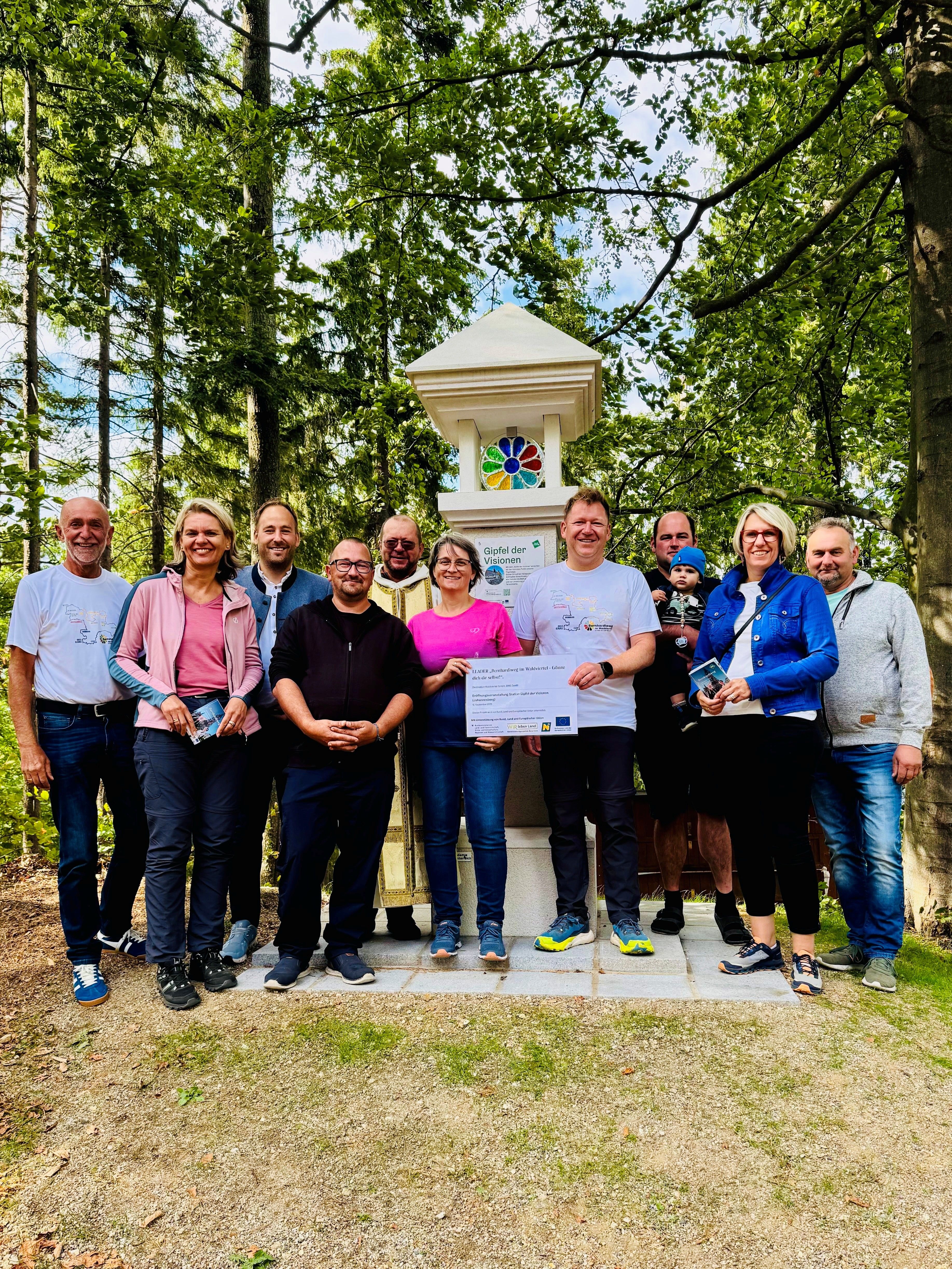 Eine Gruppe aus Männern und Frauen stehen vor dem neu aufgestellten Marterl bei der Station "Gipfel der Visionen" am Johannesberg. Die Station ist Teil vom Pilgerweg Bernhardiweg.