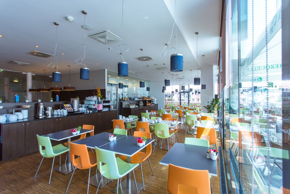 Moderner Frühstücksraum mit bunten Stühlen und gedeckten Tischen.