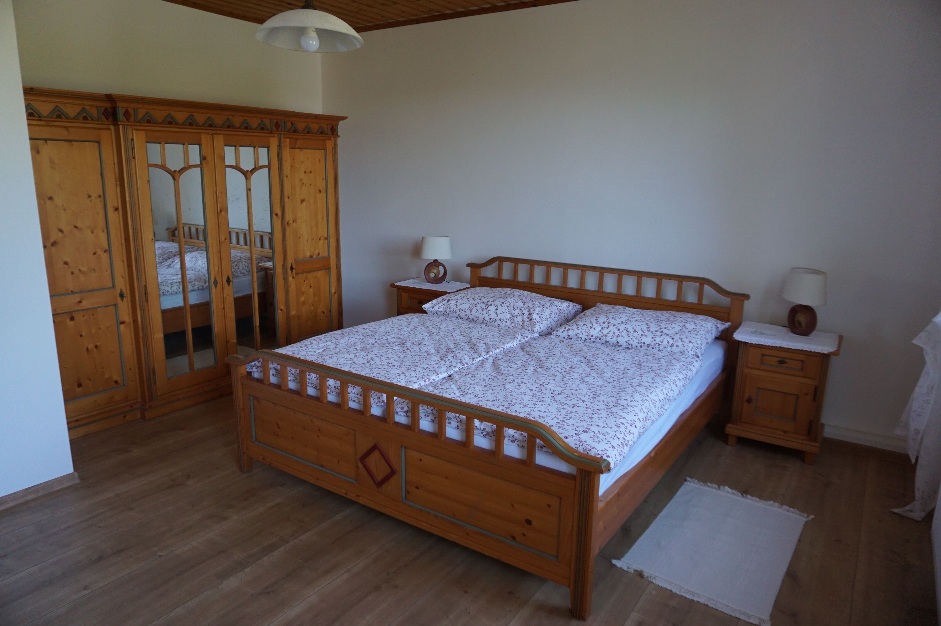 Ein Schlafzimmer mit einem Doppelbett aus Holz, einem Kleiderschrank mit Spiegeln und zwei Nachttischen mit Lampen.