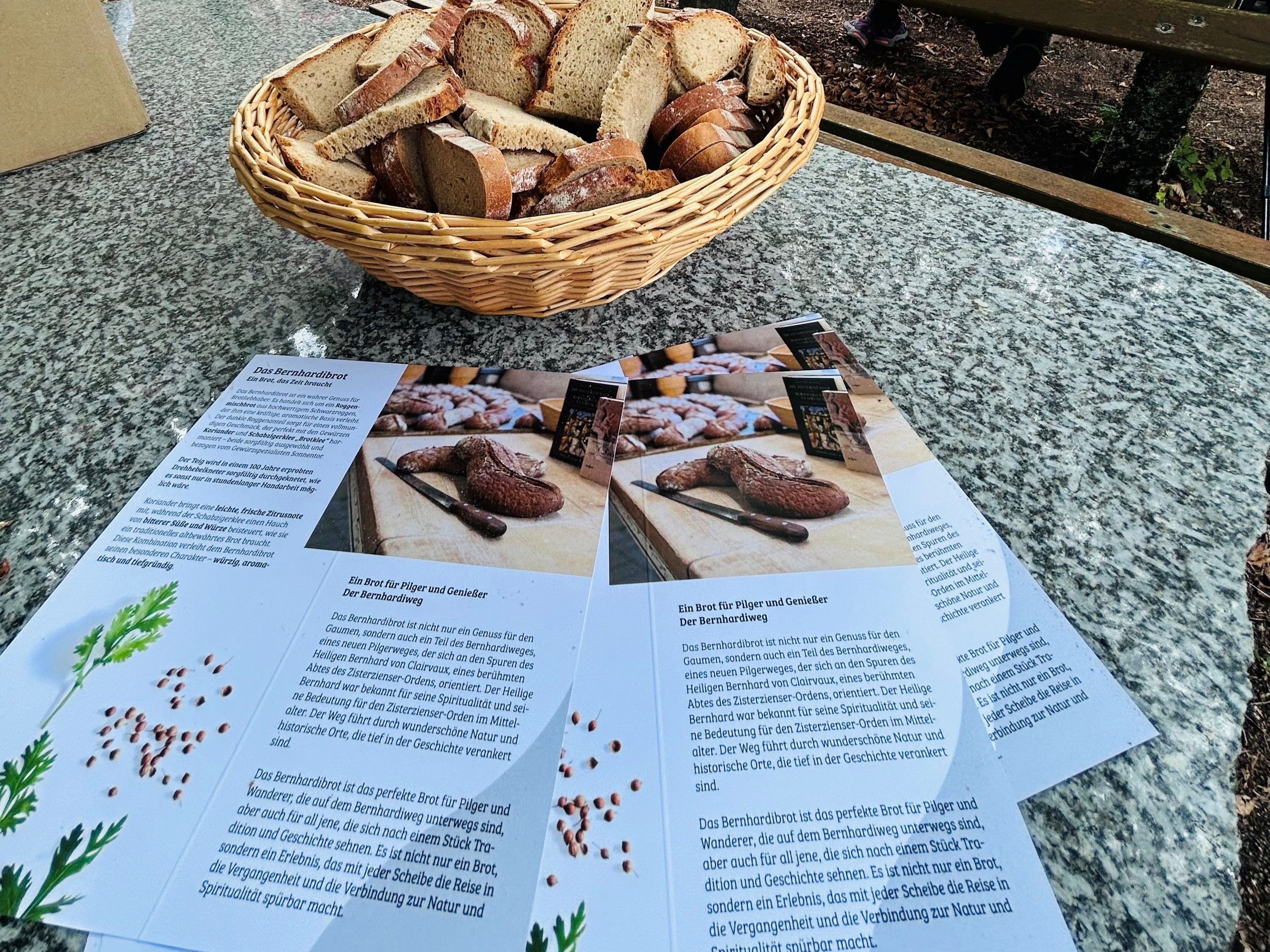 Aufgeschnittenes Brot ist in einem Körbchen angerichtet und steht zur freien Verfügung, daneben liegt eine Broschüre die zeigt, dass das Brot das Bernhardibrot ist mit weiteren Informationen dazu. Anlass ist die Segnung des Marterls Gipfel der Visionen am Pilgerweg Bernhardiweg im Waldviertel.