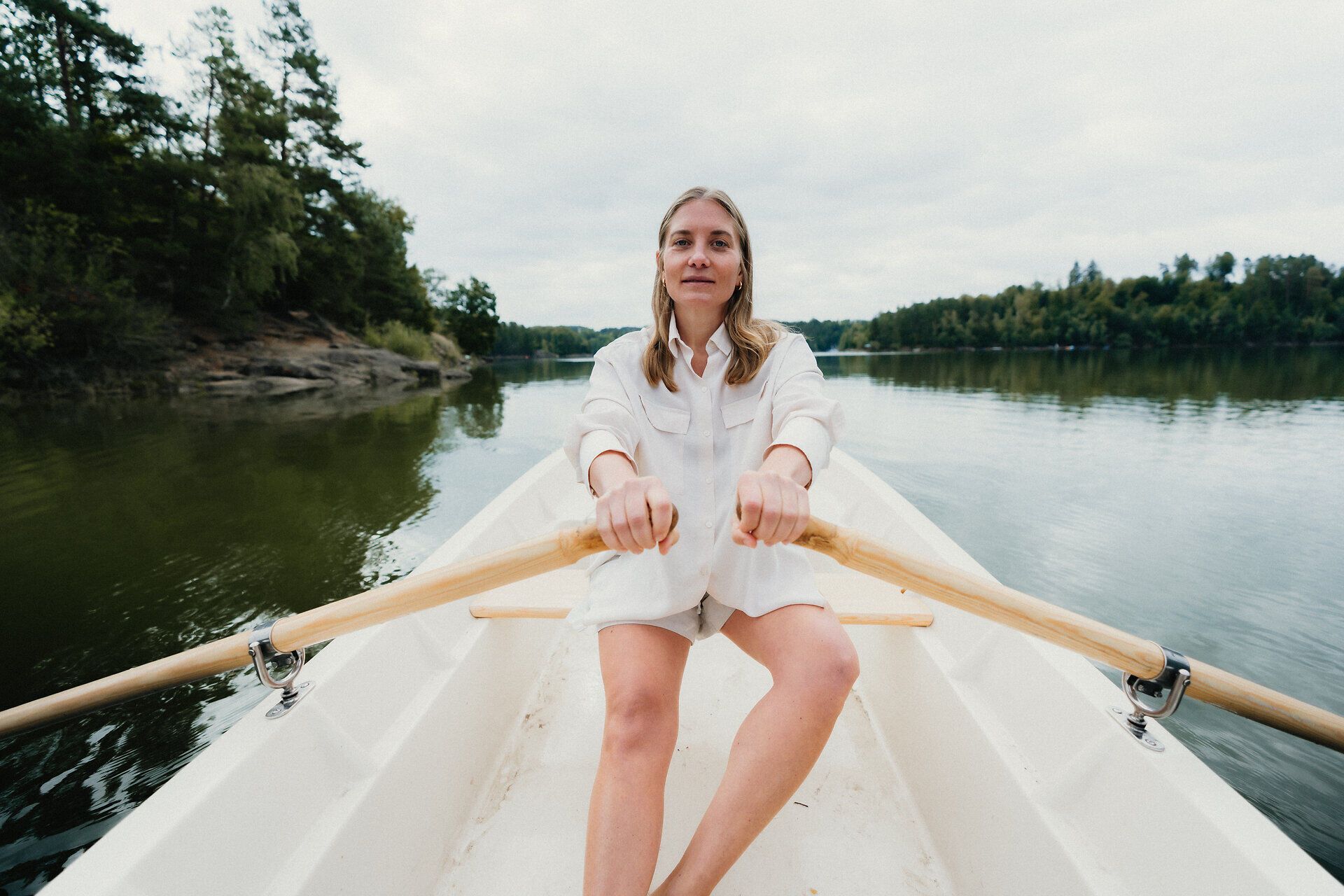 Eine Frau rudert in einem weißen Ruderboot über den Stausee Ottenstein im Waldviertel. Rund um das ruhige Wasser sind bewaldete Ufer und Felsen zu sehen.