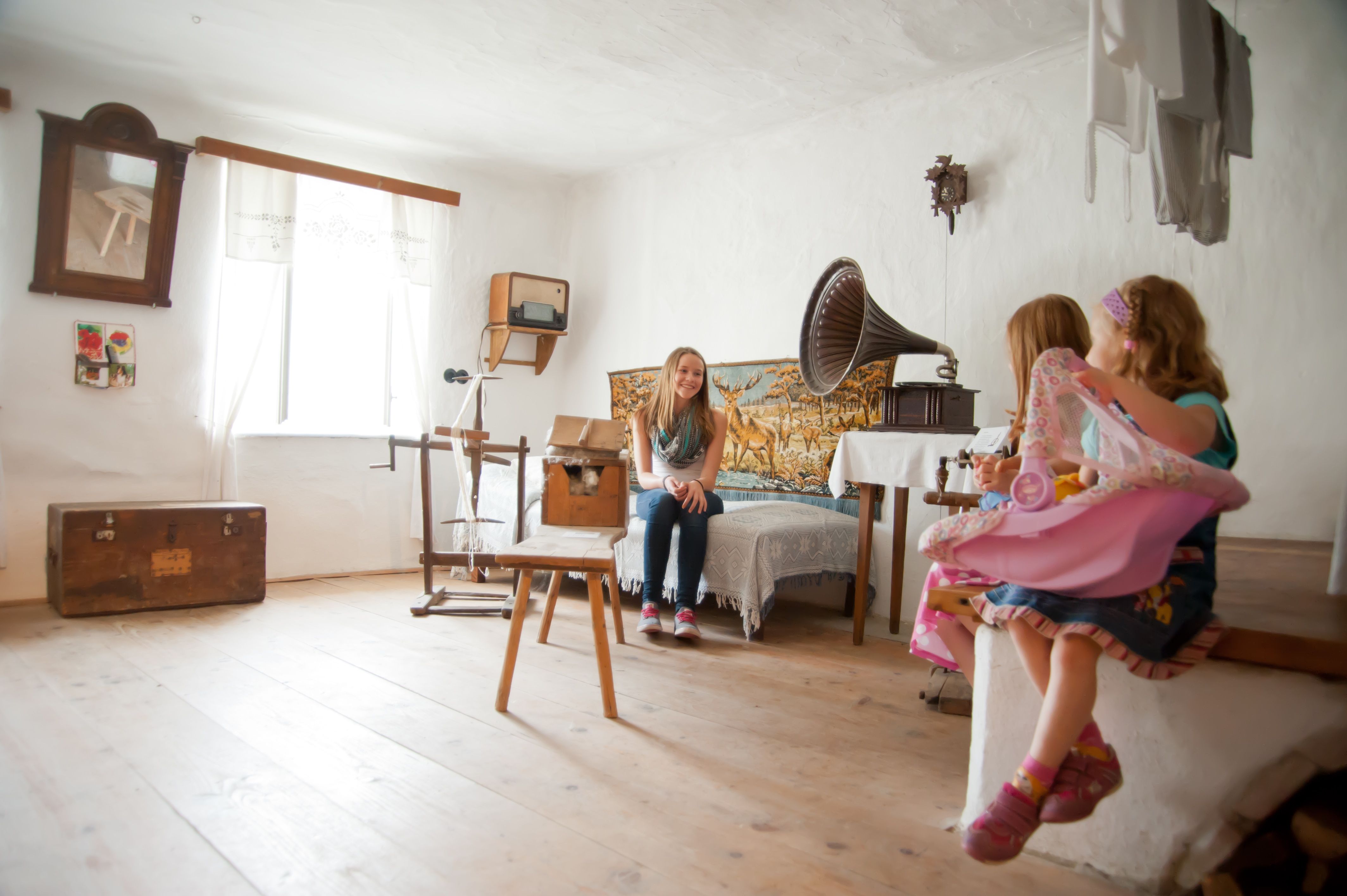 Ein Raum im Freizeitmuseum Langau mit antiken Möbeln und einem Grammophon. Zwei Kinder sitzen auf einer Bank, ein Mädchen sitzt auf einem Bett.