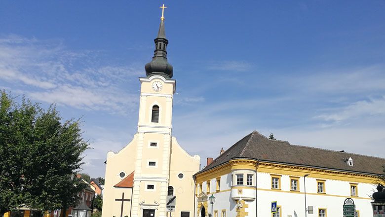 Pfarrkirche mit Turm und angrenzendem Pfarrhof bei klarem Himmel.