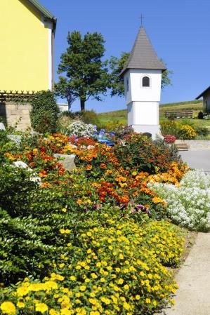Ein blühender Garten mit bunten Blumen vor einem kleinen, weißen Kapellengebäude.