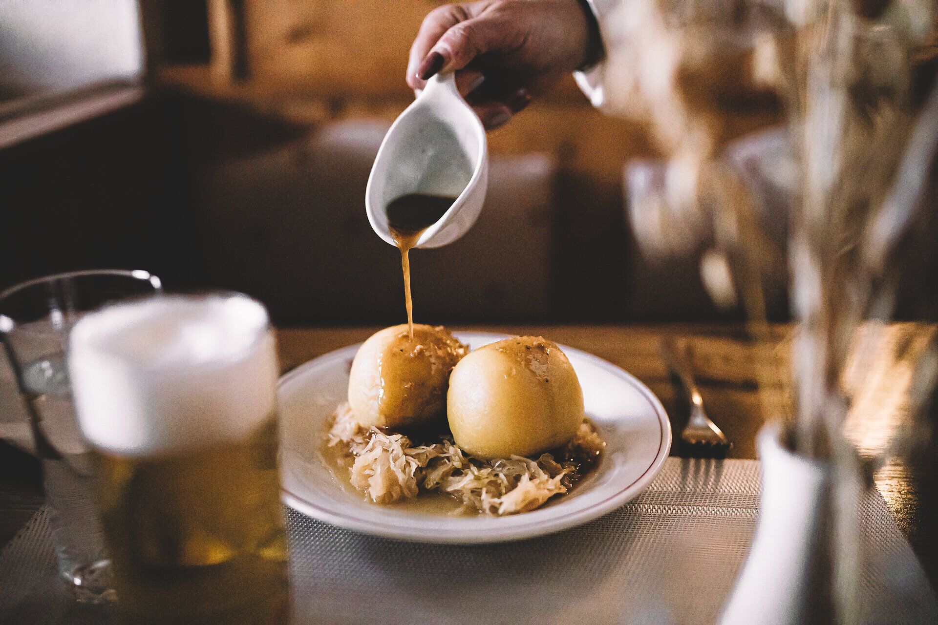 Ein köstlicher Fleischknödel wird mit einer aromatischen Sauce serviert, während ein kühles Bier auf dem Tisch steht. Die rustikale Atmosphäre des Gasthofs lädt dazu ein, die traditionelle Wirtshauskultur zu genießen und sich in der herzlichen Gastfreundschaft zu verlieren.