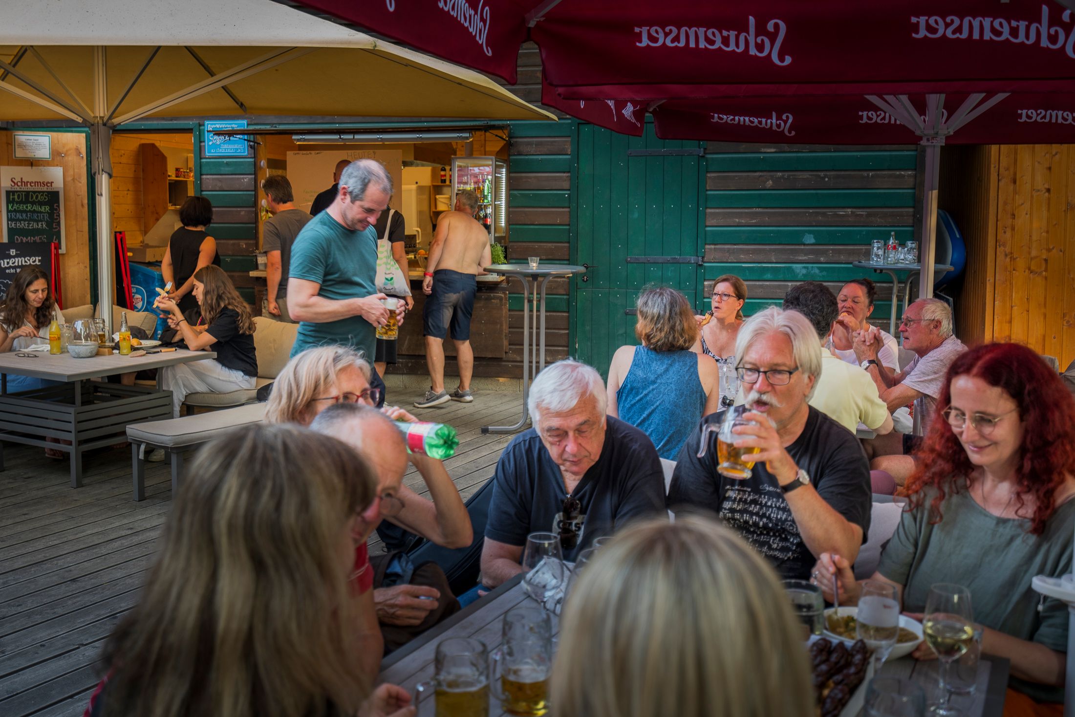 Menschen sitzen an Tischen in einem Biergarten und genießen Getränke und Snacks.