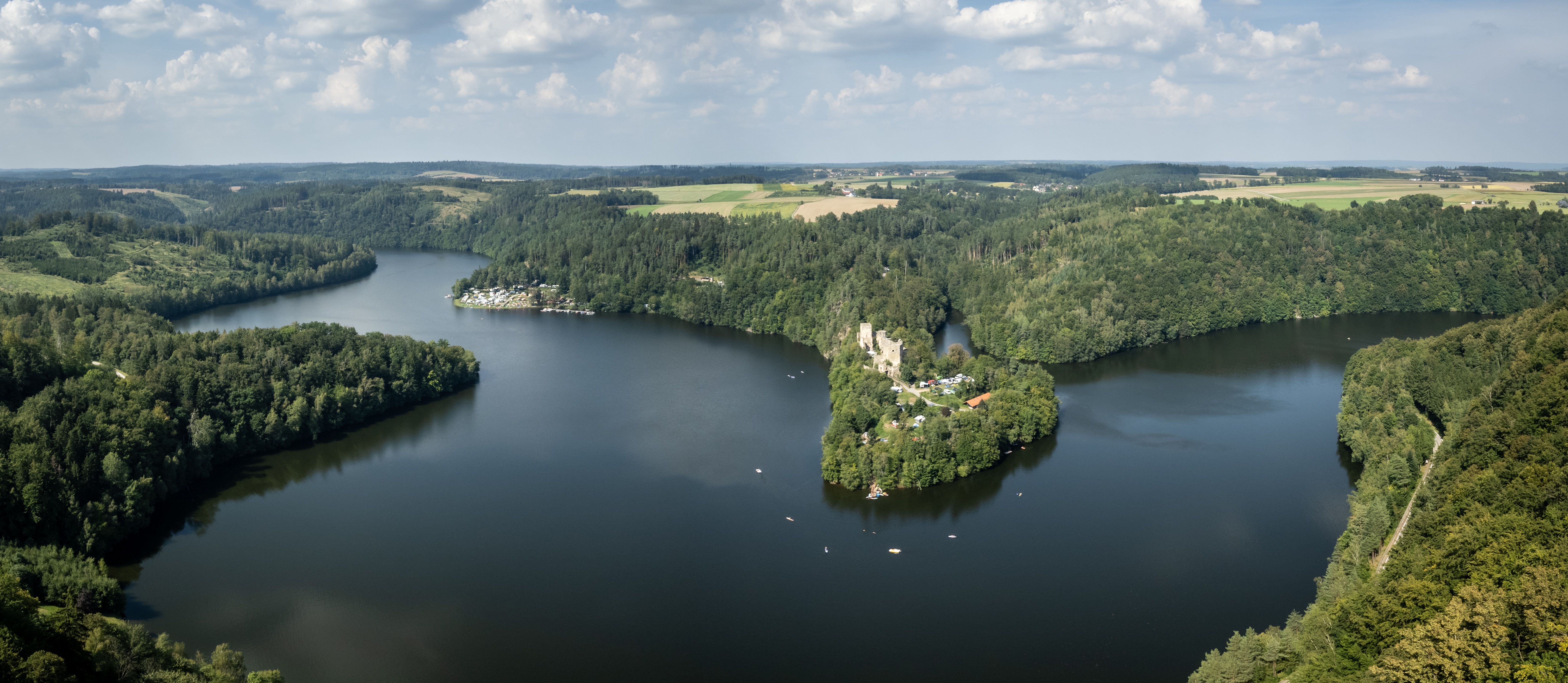 Luftaufnahme von einem Stausee umringt von grünen Wäldern und einer Ruine auf einer Halbinsel