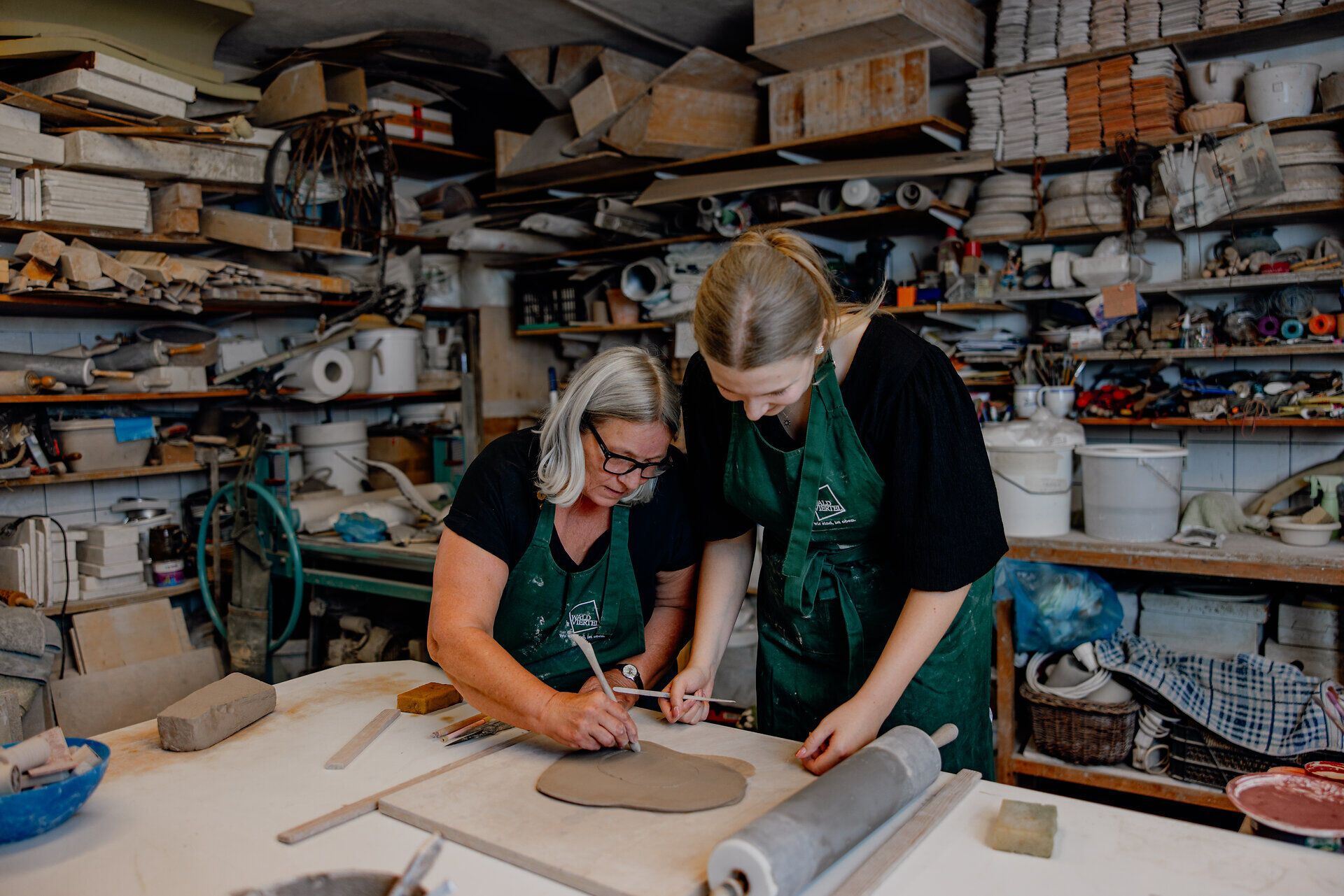 In der kreativen Atmosphäre von Keramik Hrouza arbeiten zwei Frauen konzentriert an ihren Kunstwerken. Der Raum ist erfüllt von der Wärme des Tons und dem Duft von frischer Erde, während sie mit Leidenschaft und Geschick ihre Ideen zum Leben erwecken.