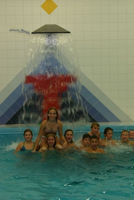 Gruppe von Kindern im Hallenbad unter einem Wasserfall.
