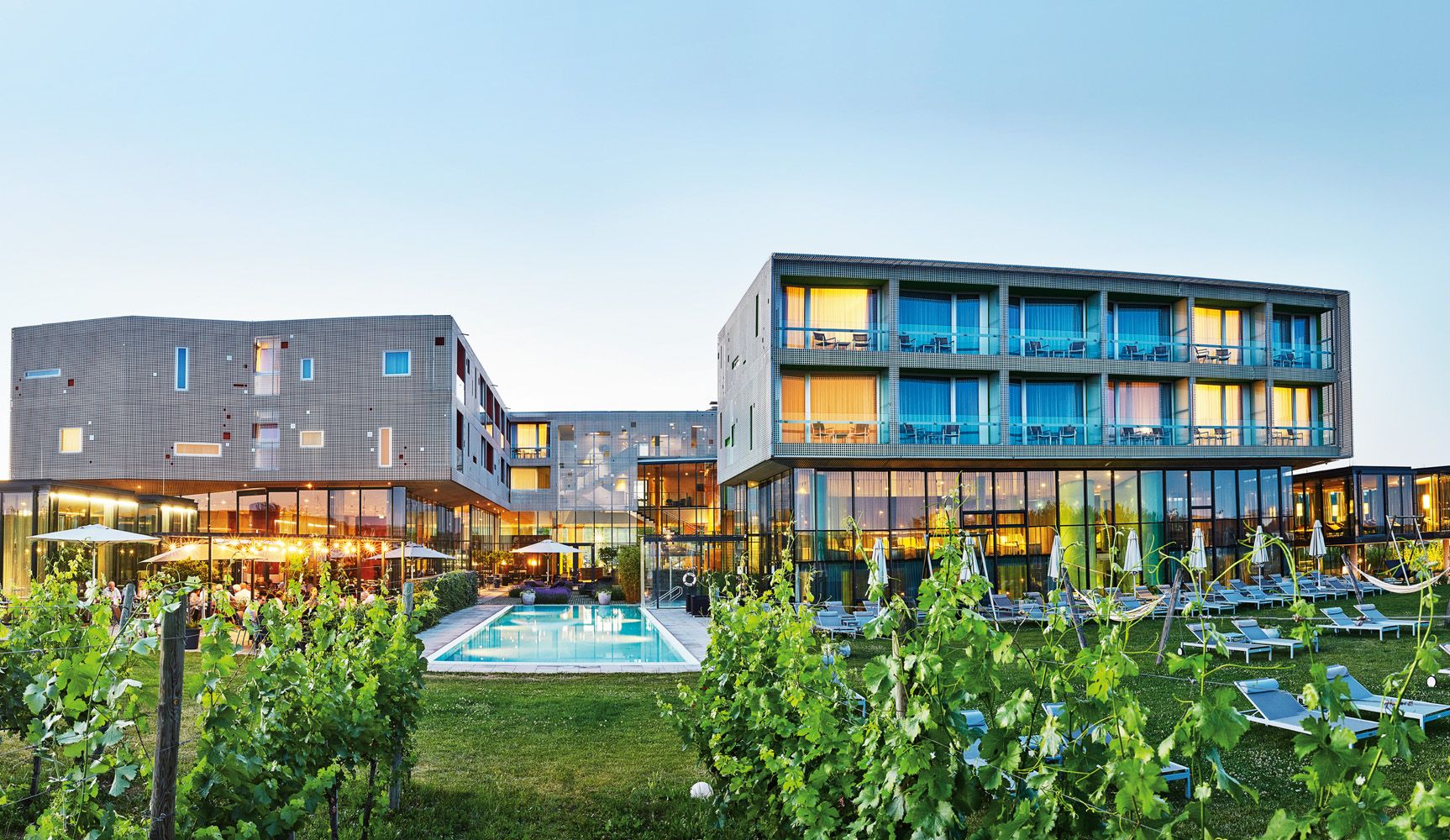 Modernes Hotelgebäude mit Pool und Weinreben im Vordergrund.