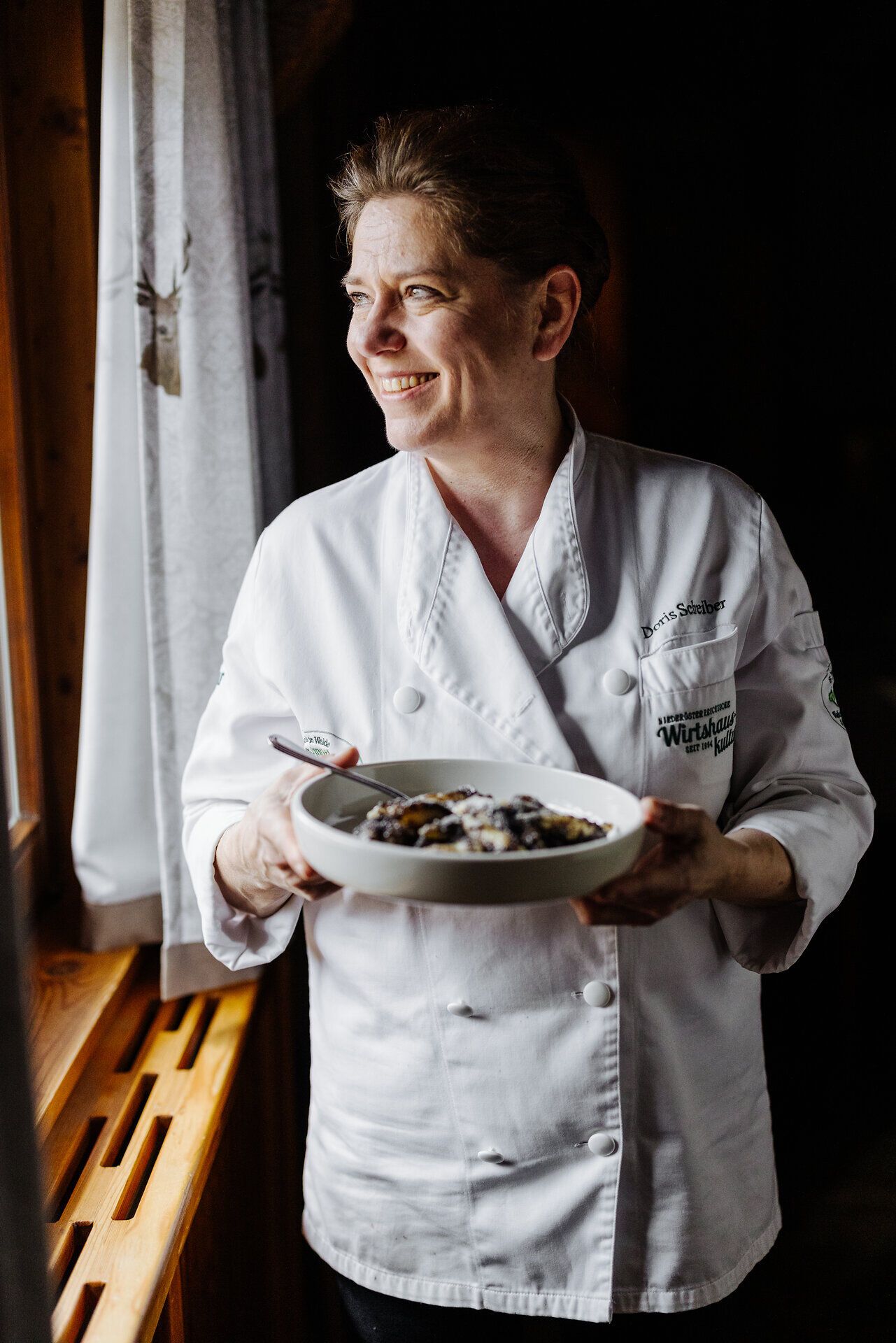 In der gemütlichen Waldschenke Schreiber strahlt die Köchin Doris Schreiber mit einem Teller köstlicher Mohnnudeln, während das sanfte Licht durch das Fenster fällt. Die Atmosphäre ist warm und einladend, perfekt für eine entspannte Auszeit in der Natur.