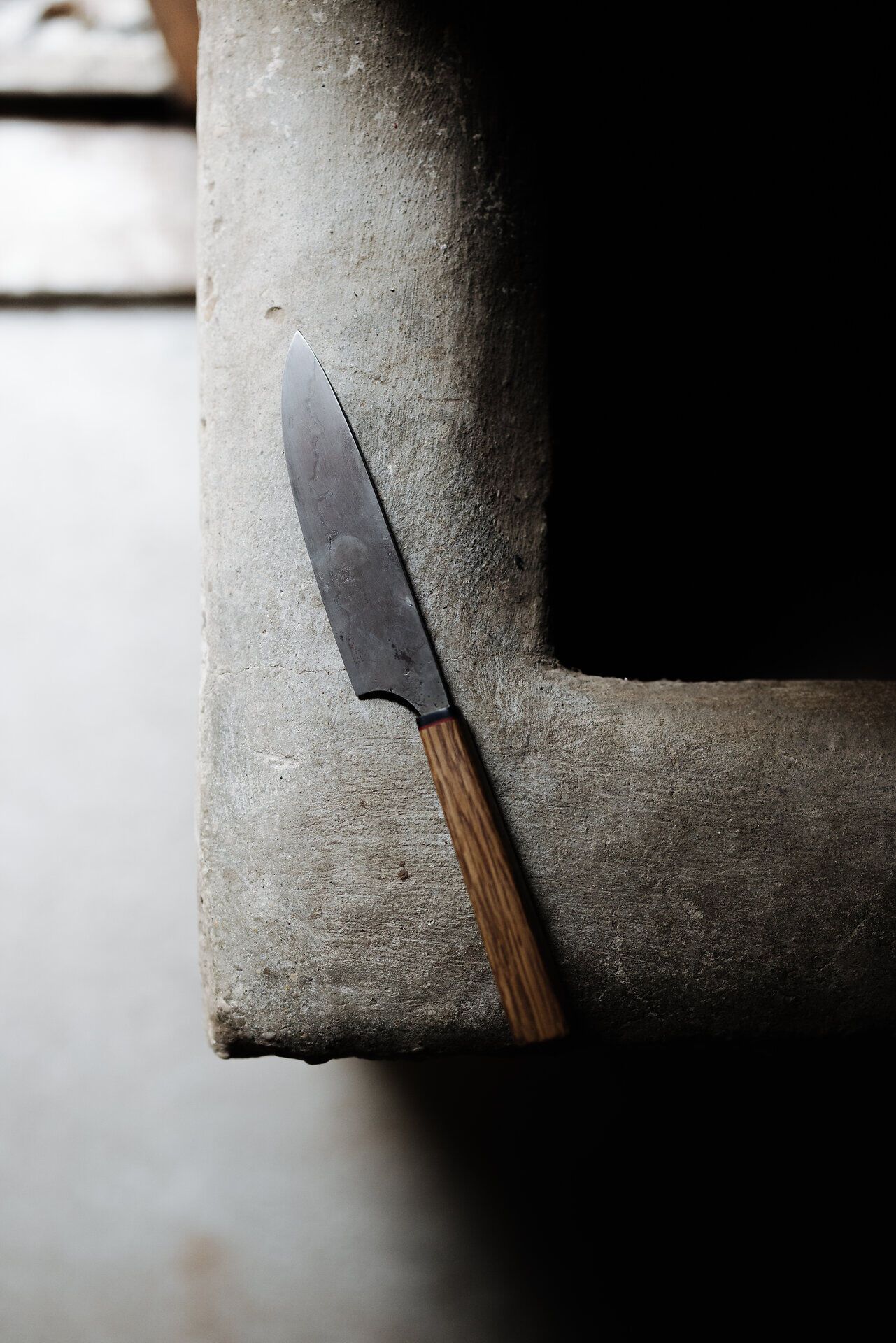 Ein handgefertigtes Messer liegt elegant auf einer rustikalen Steinoberfläche. Die Kombination aus dem schimmernden Stahl und dem warmen Holzgriff vermittelt ein Gefühl von Tradition und Handwerkskunst. Hier spürt man die Leidenschaft und Präzision, die in jedes Stück einfließt.