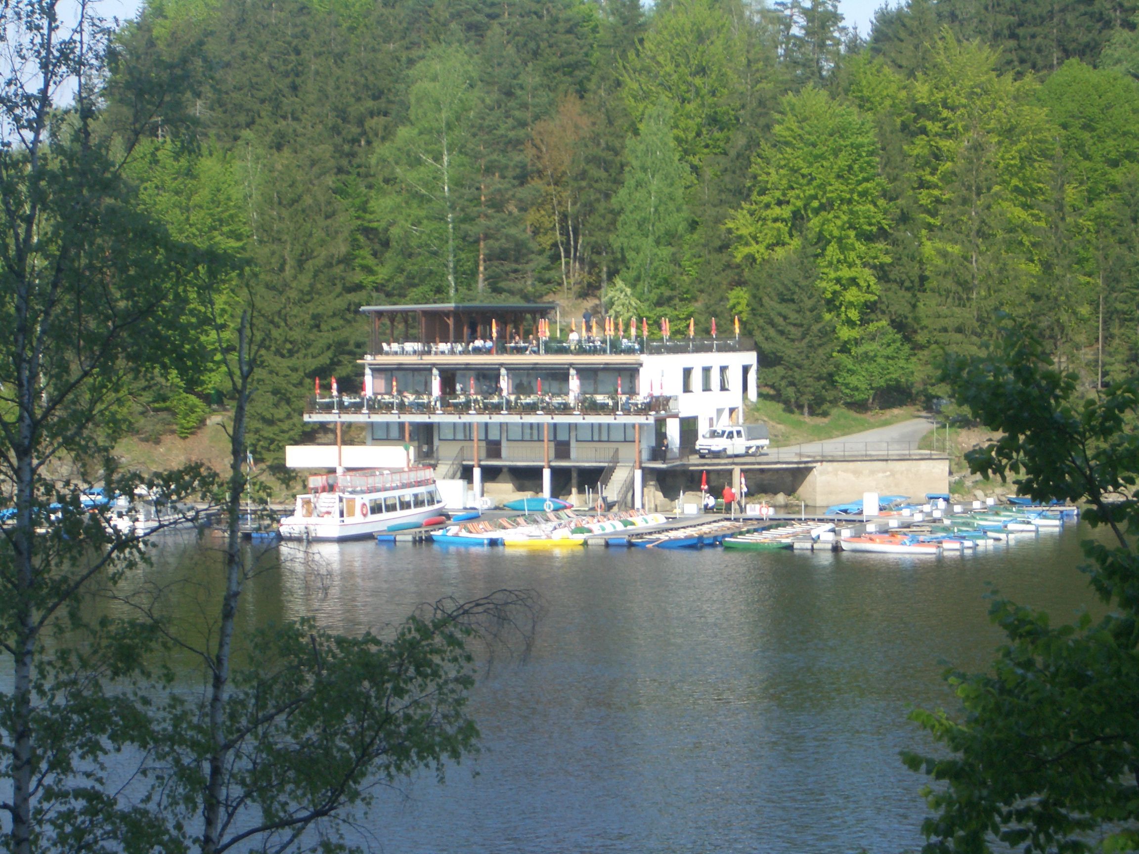 Ein Seerestaurant mit Terrasse und Bootsanleger vor einem Wald.