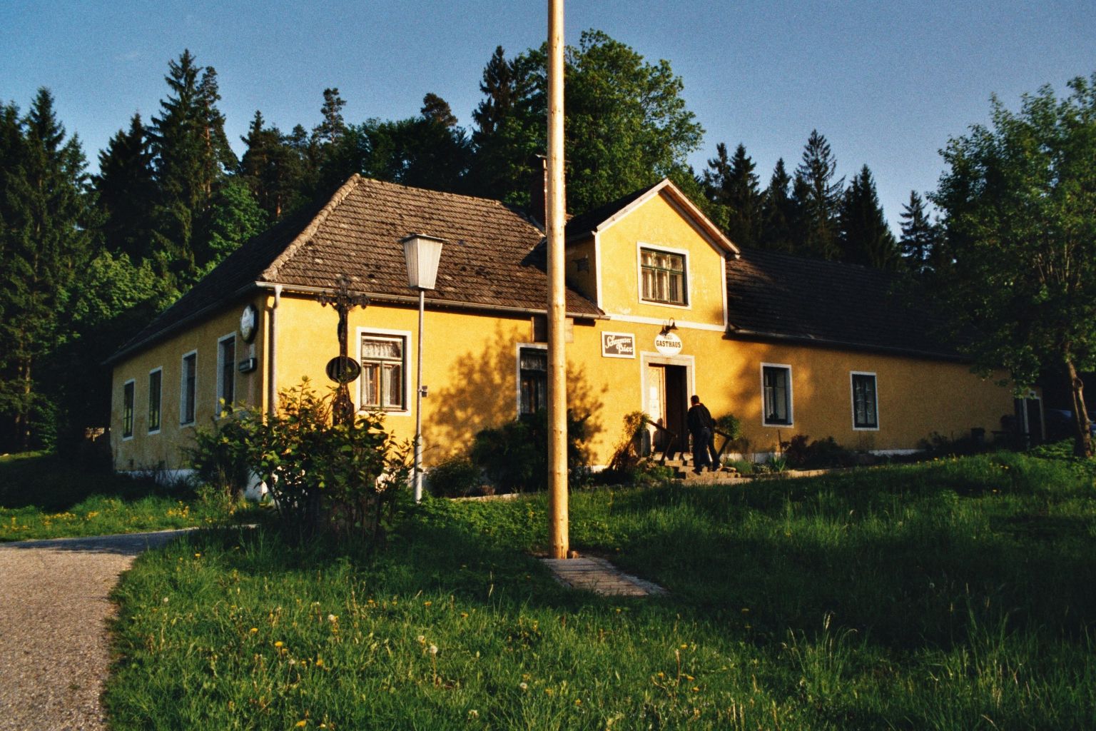 Gelbes Gasthaus in ländlicher Umgebung mit Bäumen im Hintergrund.