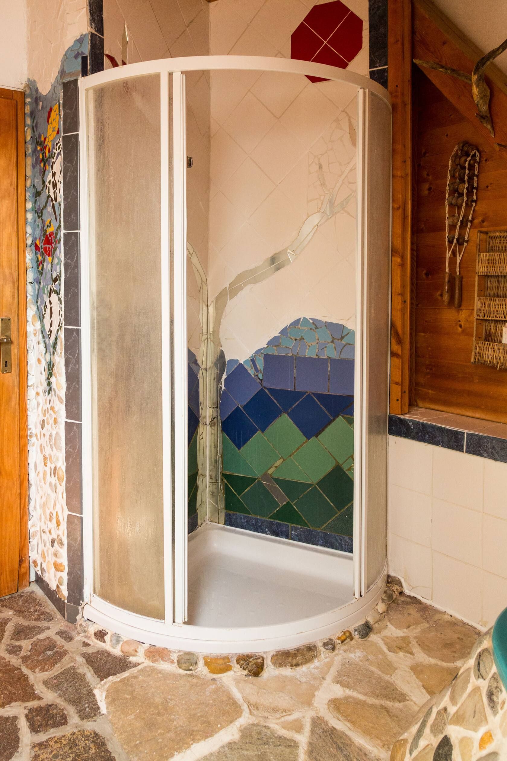 Halbrunde Duschkabine mit Milchglas, Mosaikwand und Natursteinboden in einem rustikal gestalteten Badezimmer.