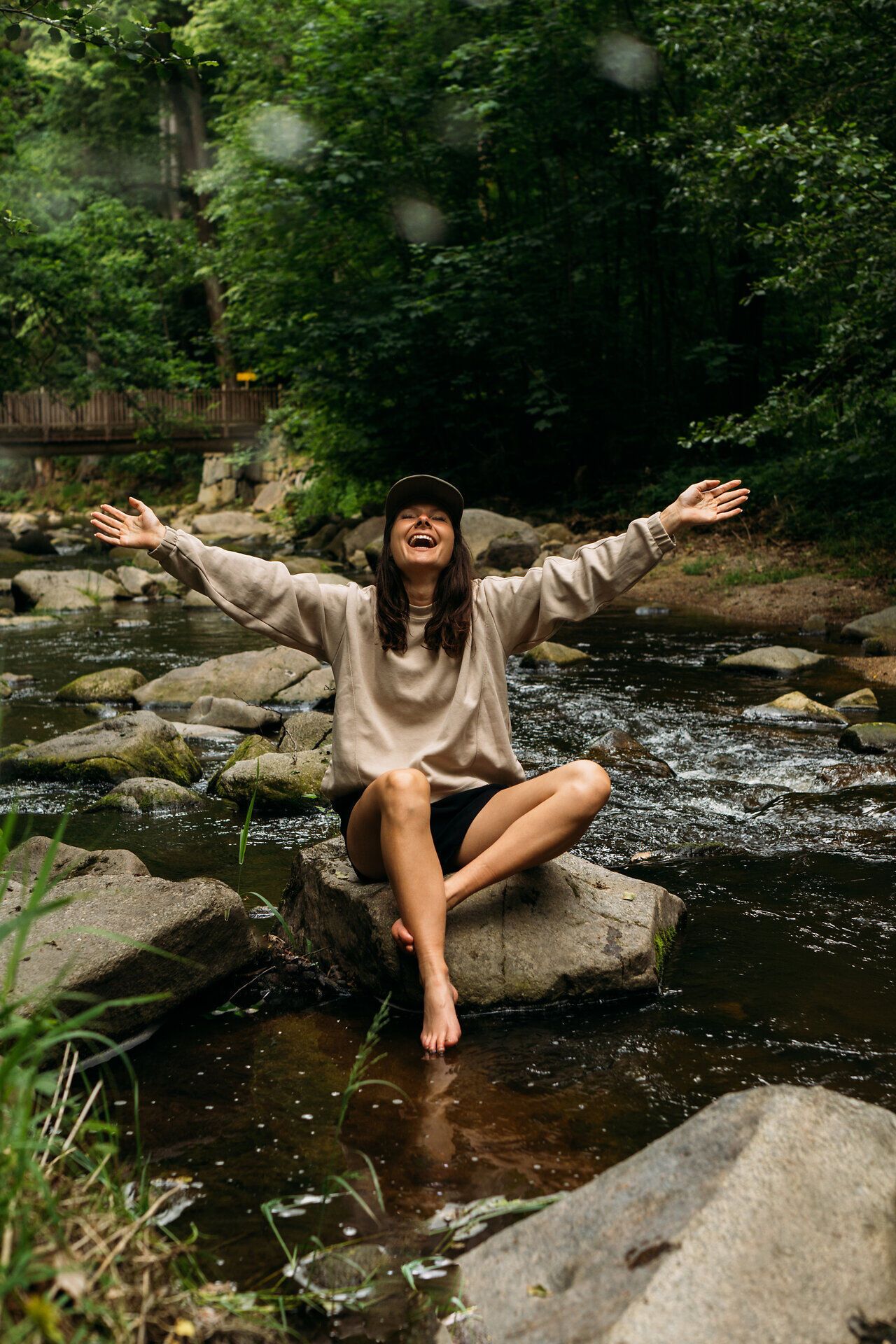 Eine Frau sitzt auf einem Felsen in einem Bach im Gabrielental, umgeben von üppigem Grün, im Waldviertel.