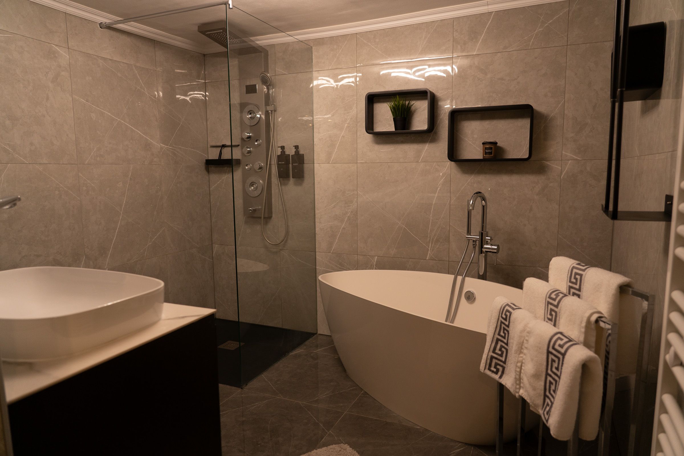 Modernes Badezimmer mit freistehender Badewanne, Glasdusche und Handtüchern auf einem Ständer.