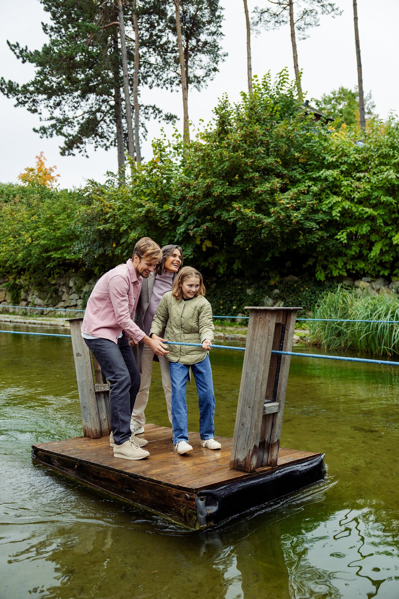 Eine Familie genießt einen unbeschwerten Moment auf einem kleinen Floß, umgeben von der idyllischen Natur der Erlebnisgärten. Die Kinder lachen und erkunden die Umgebung, während die sanften Wellen des Wassers eine friedliche Atmosphäre schaffen.
