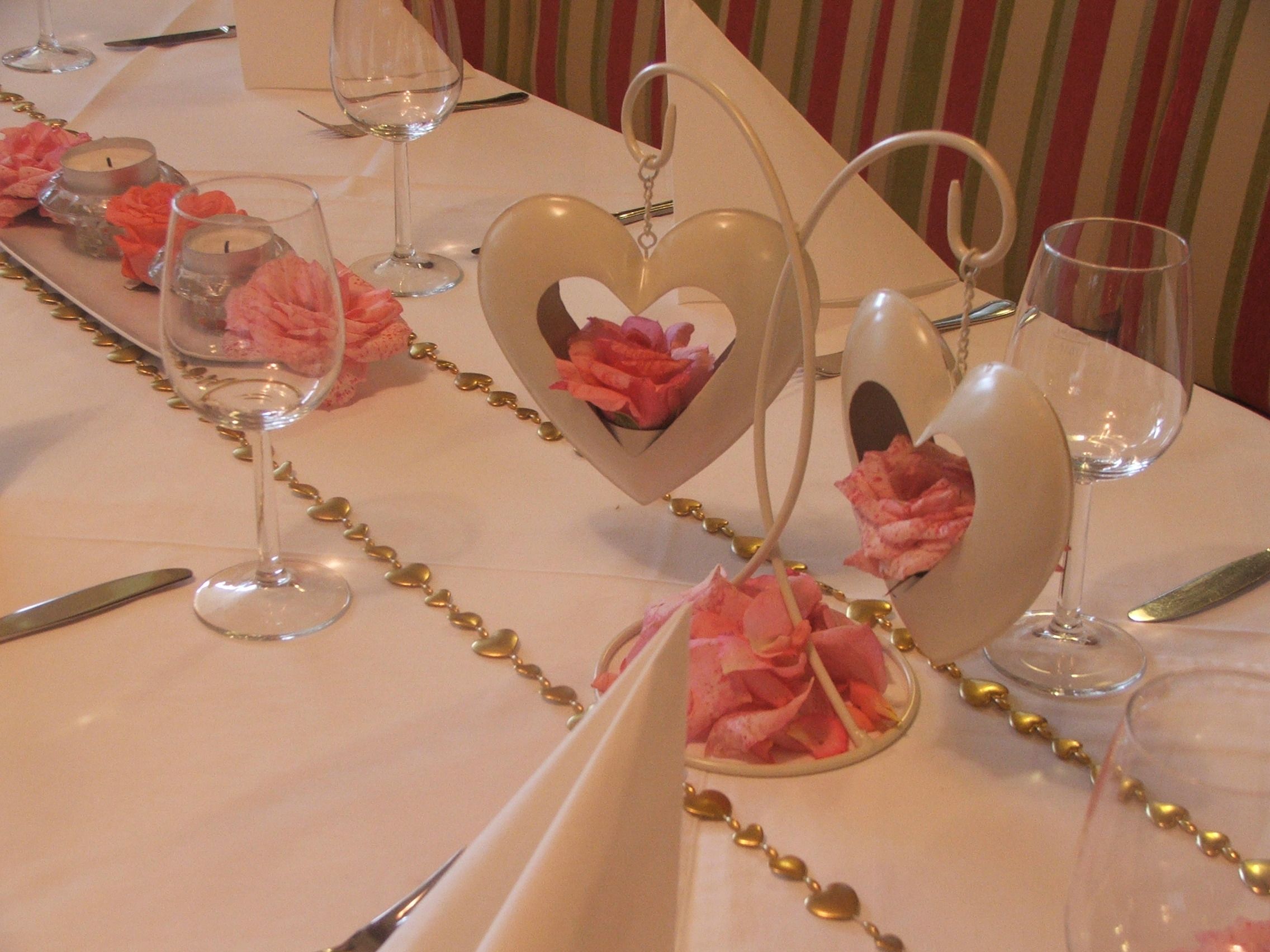 Festlich gedeckter Tisch mit Herzdekoration und Rosenblättern.