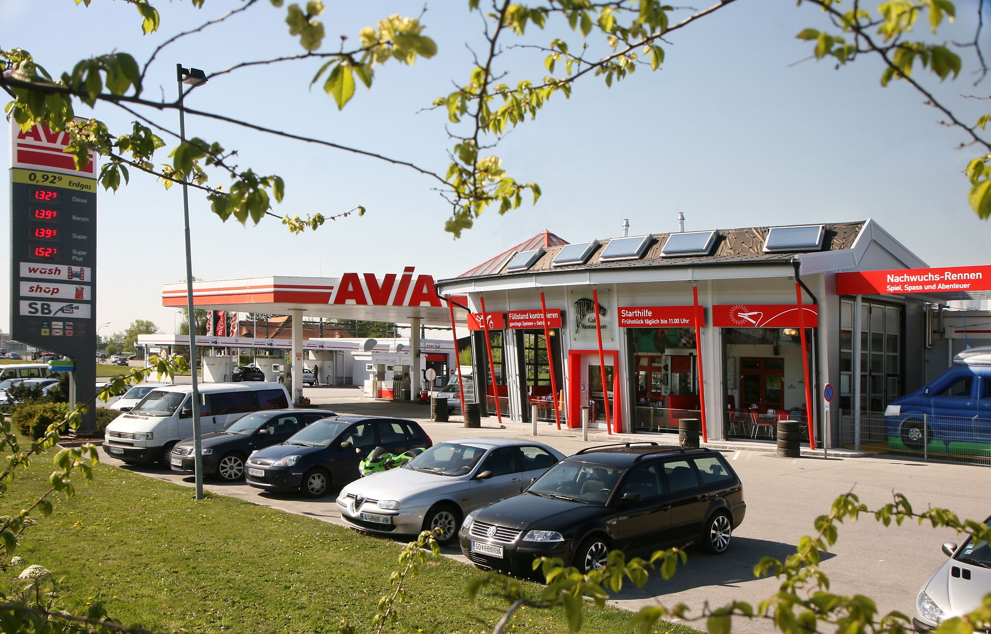 Tankstelle mit AVIA-Logo und mehreren geparkten Autos im Vordergrund.