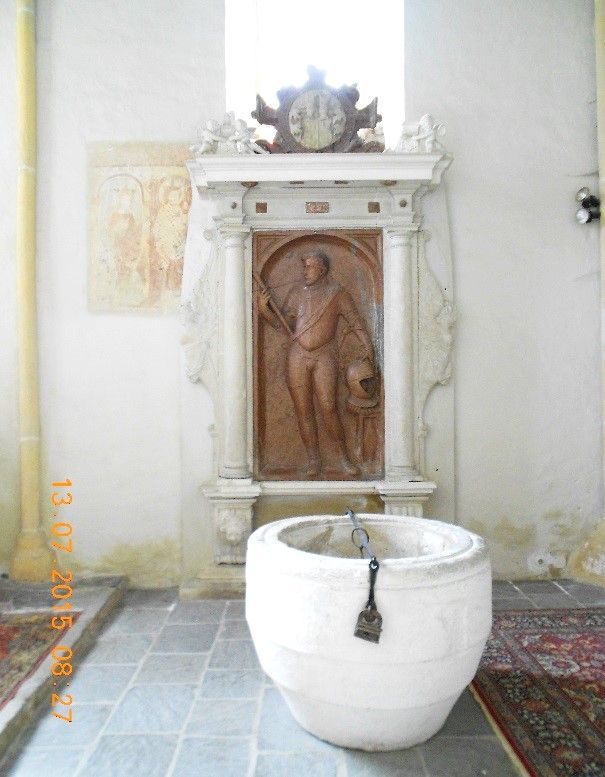 Grabmal mit Relief und Taufbecken in einer Kirche.