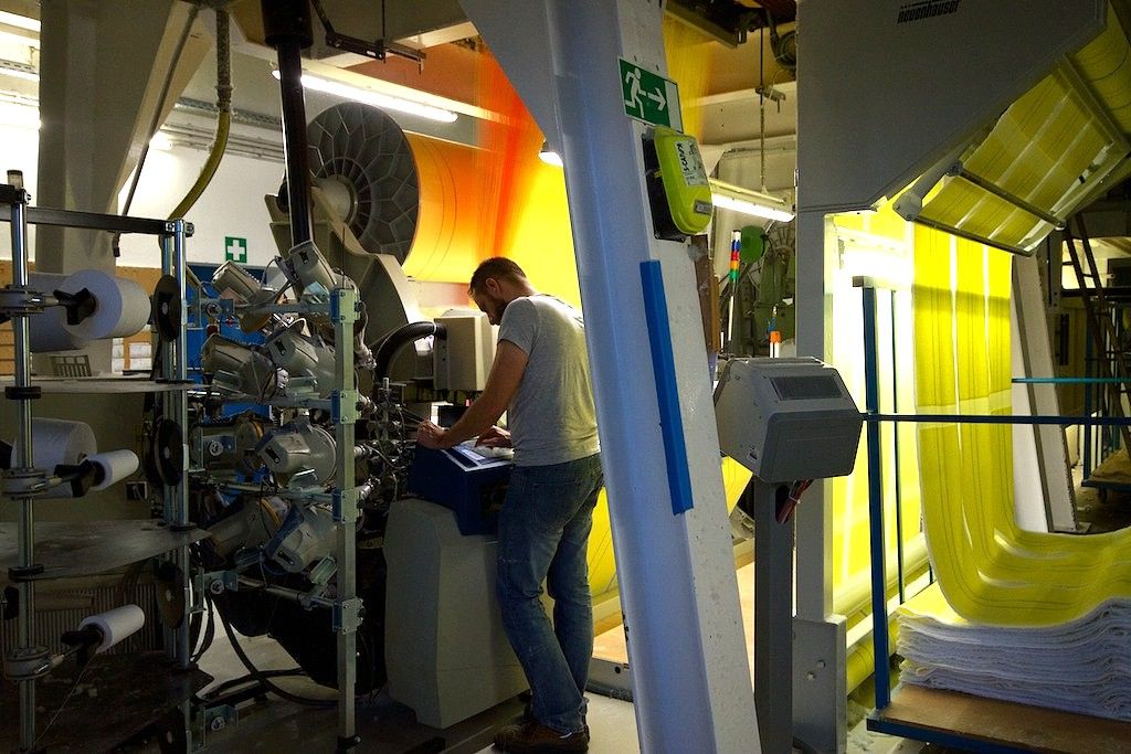 Ein Mann arbeitet an einer Maschine in einer Fabrik mit gelben und orangefarbenen Stoffbahnen.
