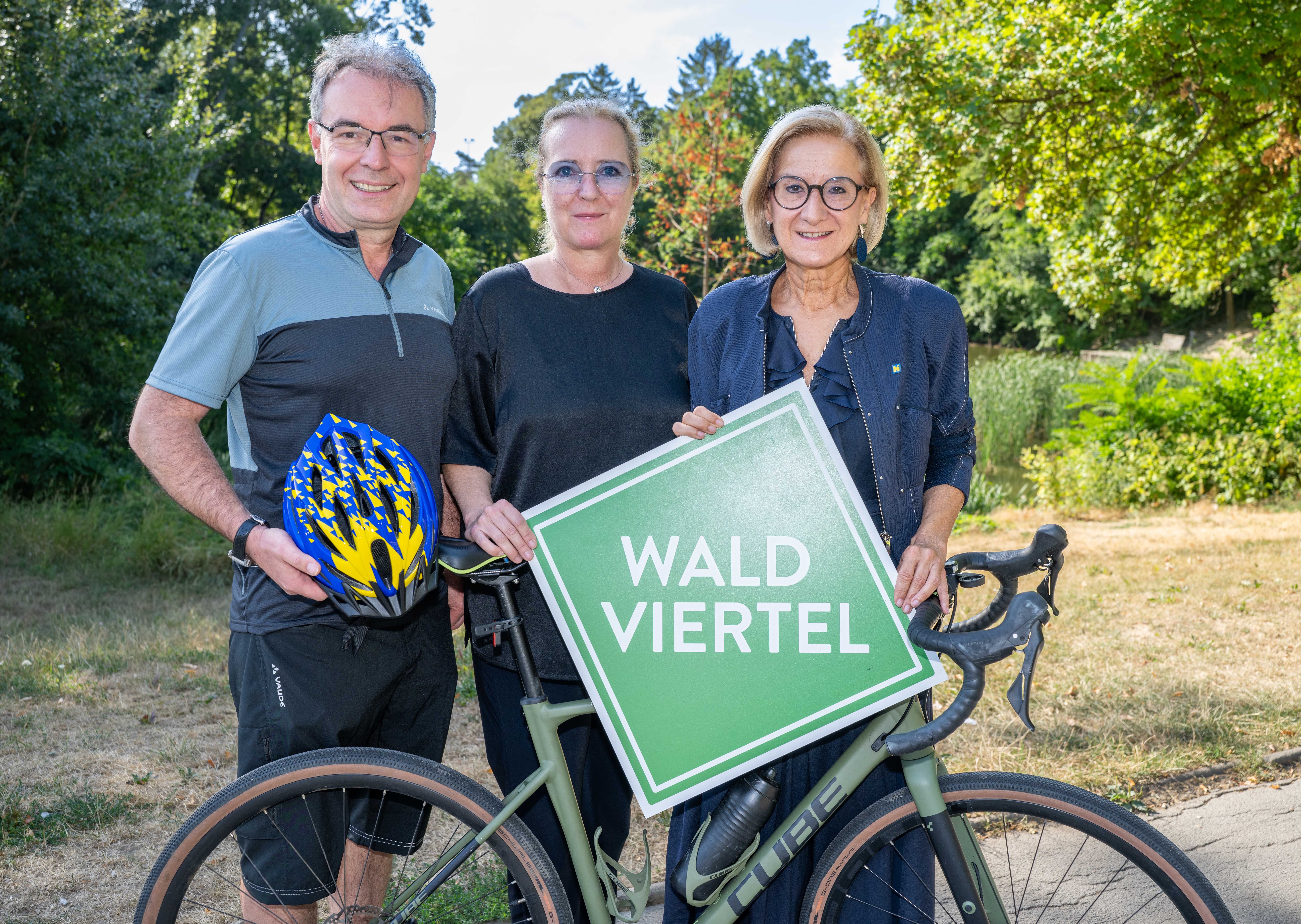 3 Menschen mit einem Rad. Eine Frau hat das Waldviertel Logo in der Hand. 