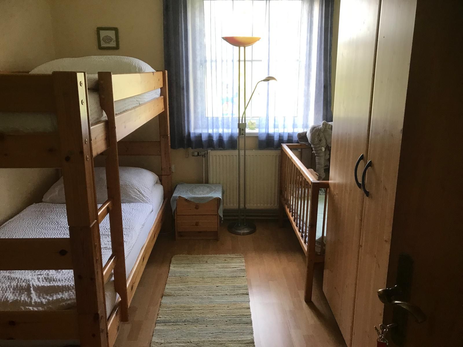 Kinderzimmer mit Etagenbett, Kinderbett, Schrank und Stehlampe.