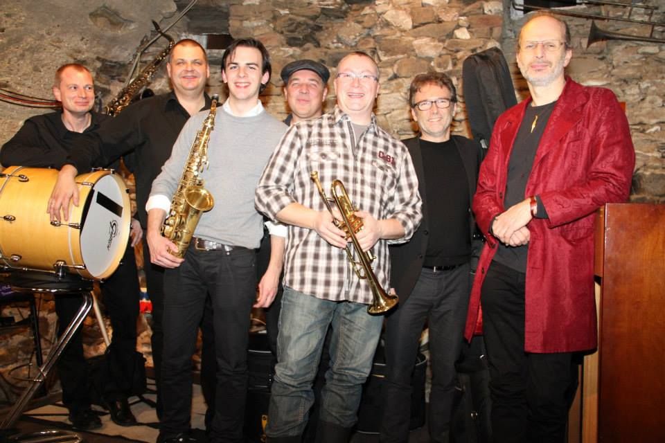 Gruppe von sieben Männern mit Musikinstrumenten in einem Jazzclub.