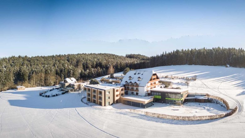 Winterlandschaft mit Hotel Schwarz Alm, umgeben von schneebedeckten Feldern und Wäldern.